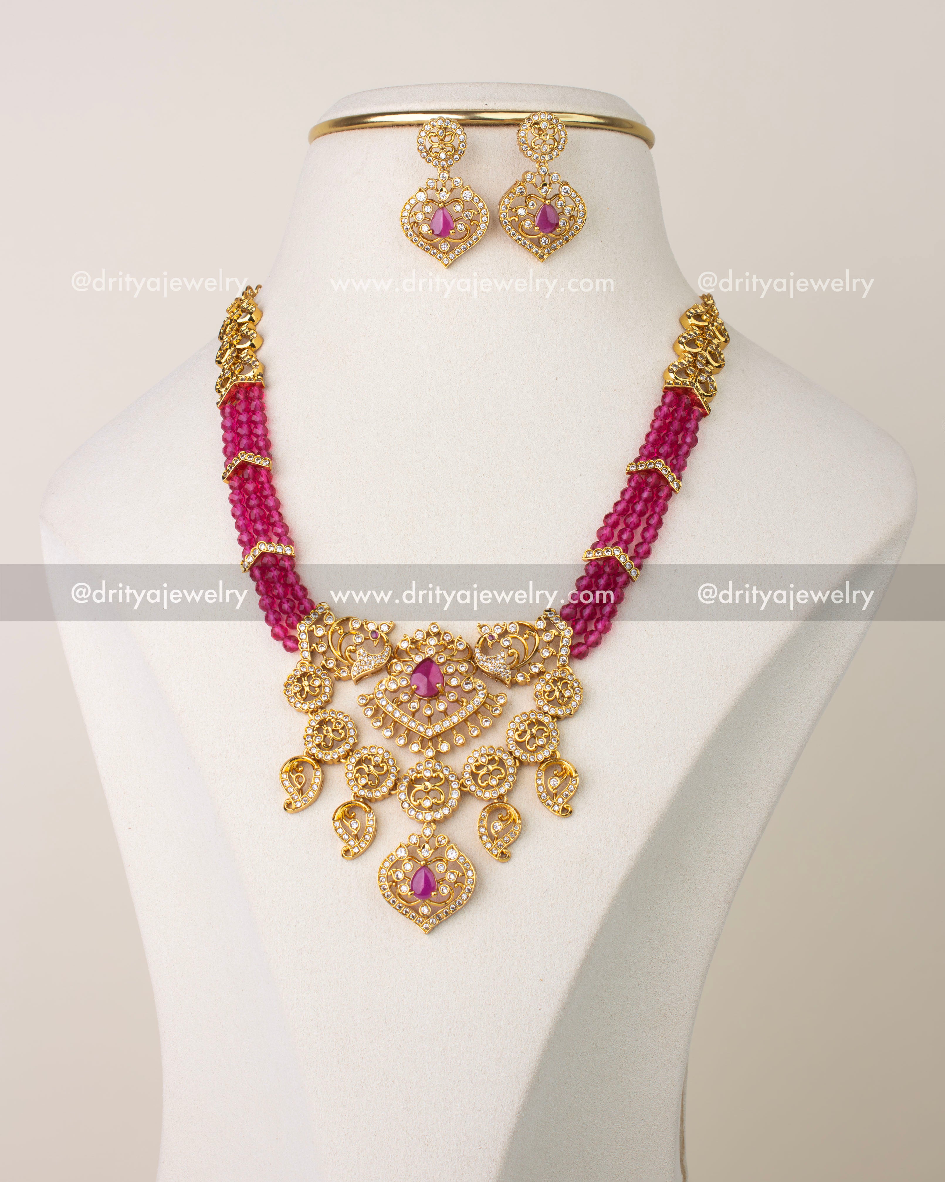 Pink beaded layered necklace set with gold-toned pendant and matching earrings on display bust.