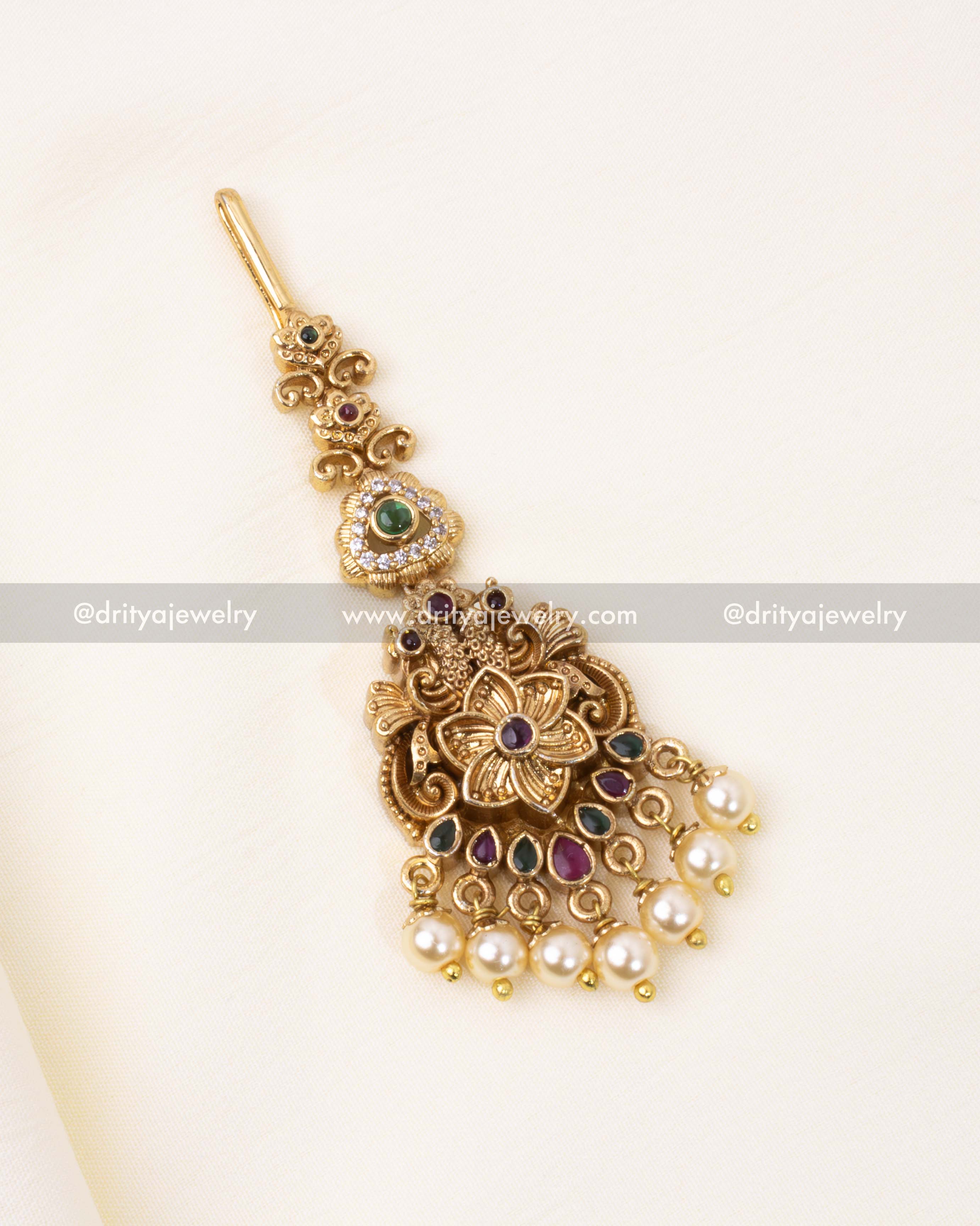A beautifully detailed antique gold Maang Tikka with floral motifs, synthetic pearls, and multi-colored stones.