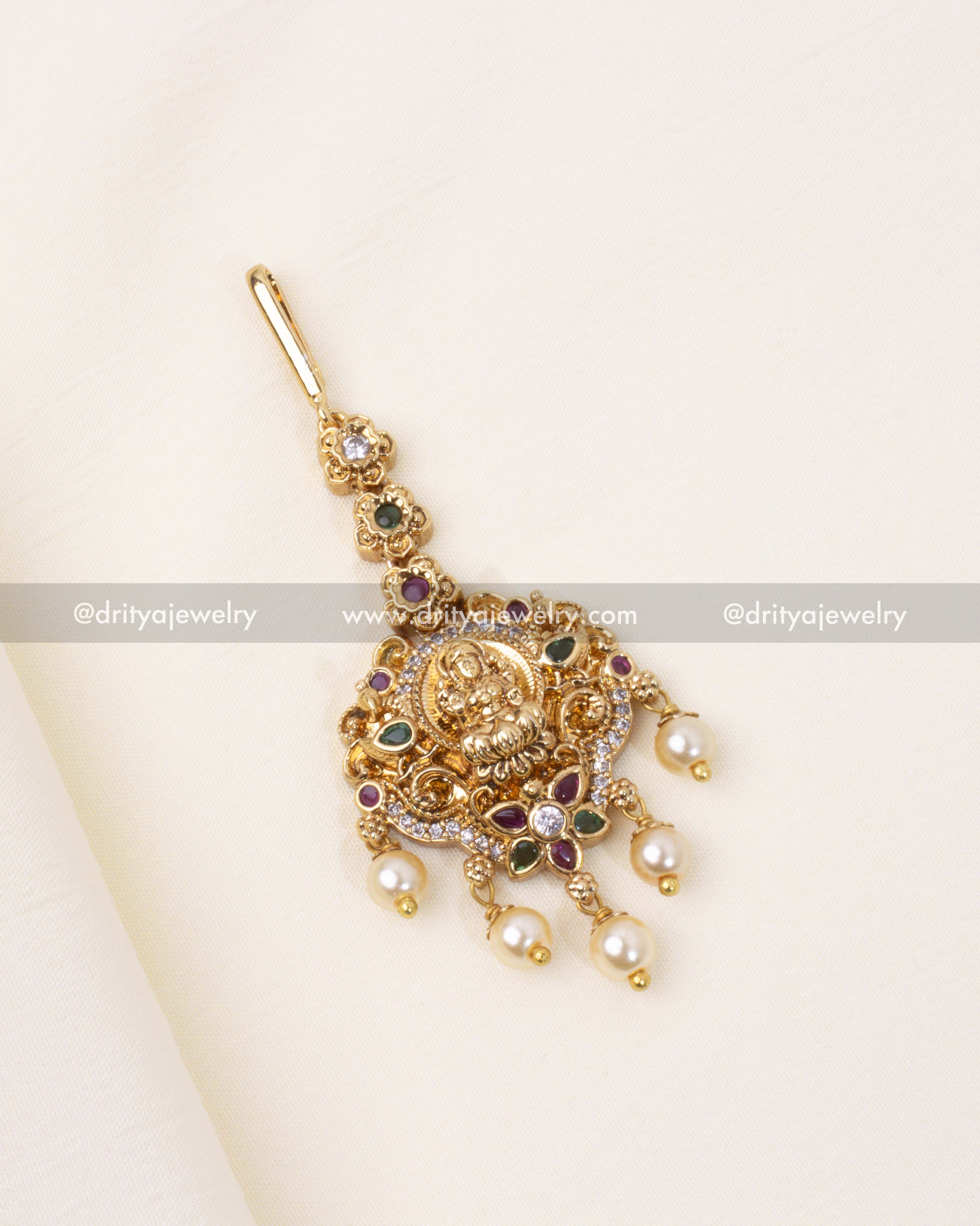 Regal Nakshi Maang Tikka featuring a Lakshmi motif, adorned with CZ stones, ruby, emerald accents, and pearl embellishments.
