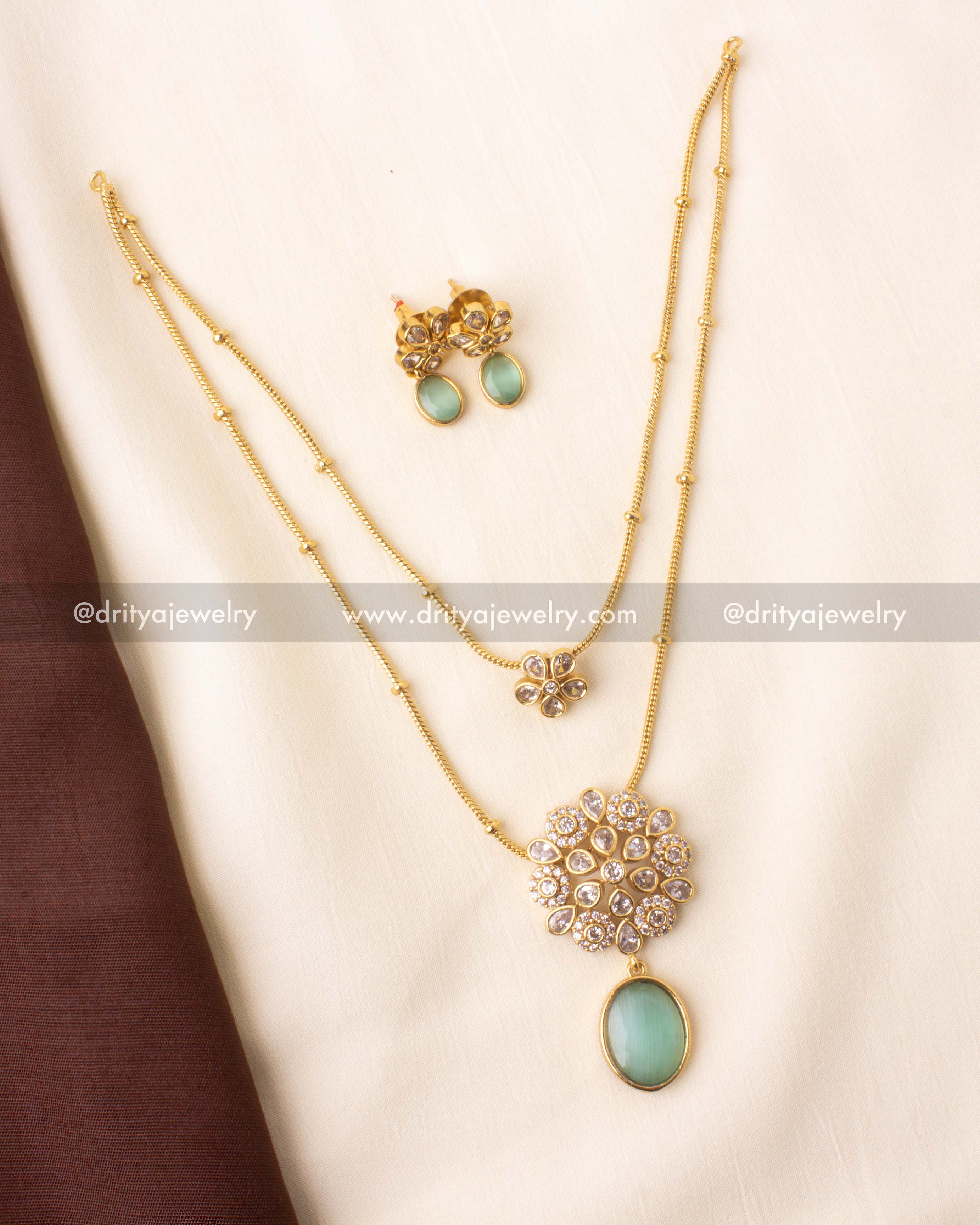Double-layered necklace with kundan floral motif and emerald green pendant.