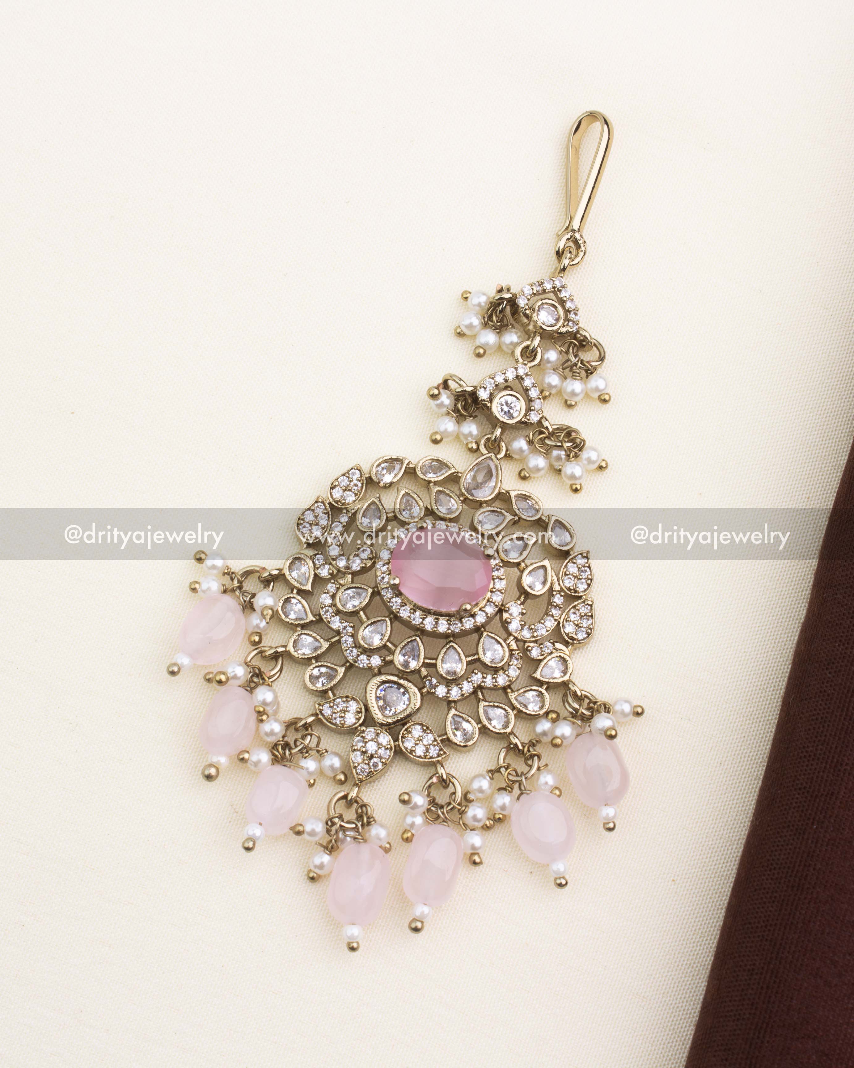 Victorian-style maang tikka with blush pink center stone, AD stones, pearl droplets, and antique gold finish.
