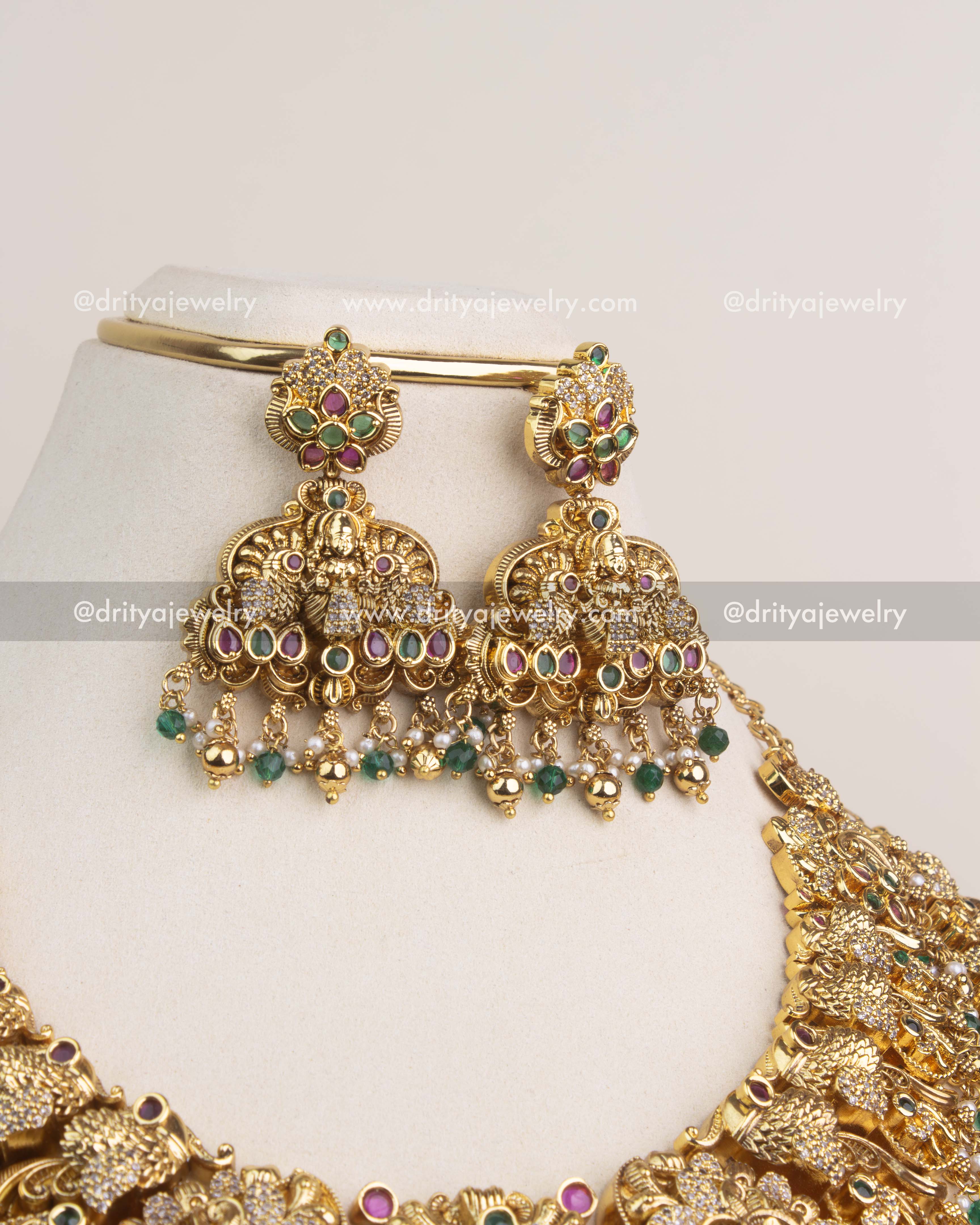 Traditional temple jhumka earrings with emerald green stone detailing and pearl bead layers.
