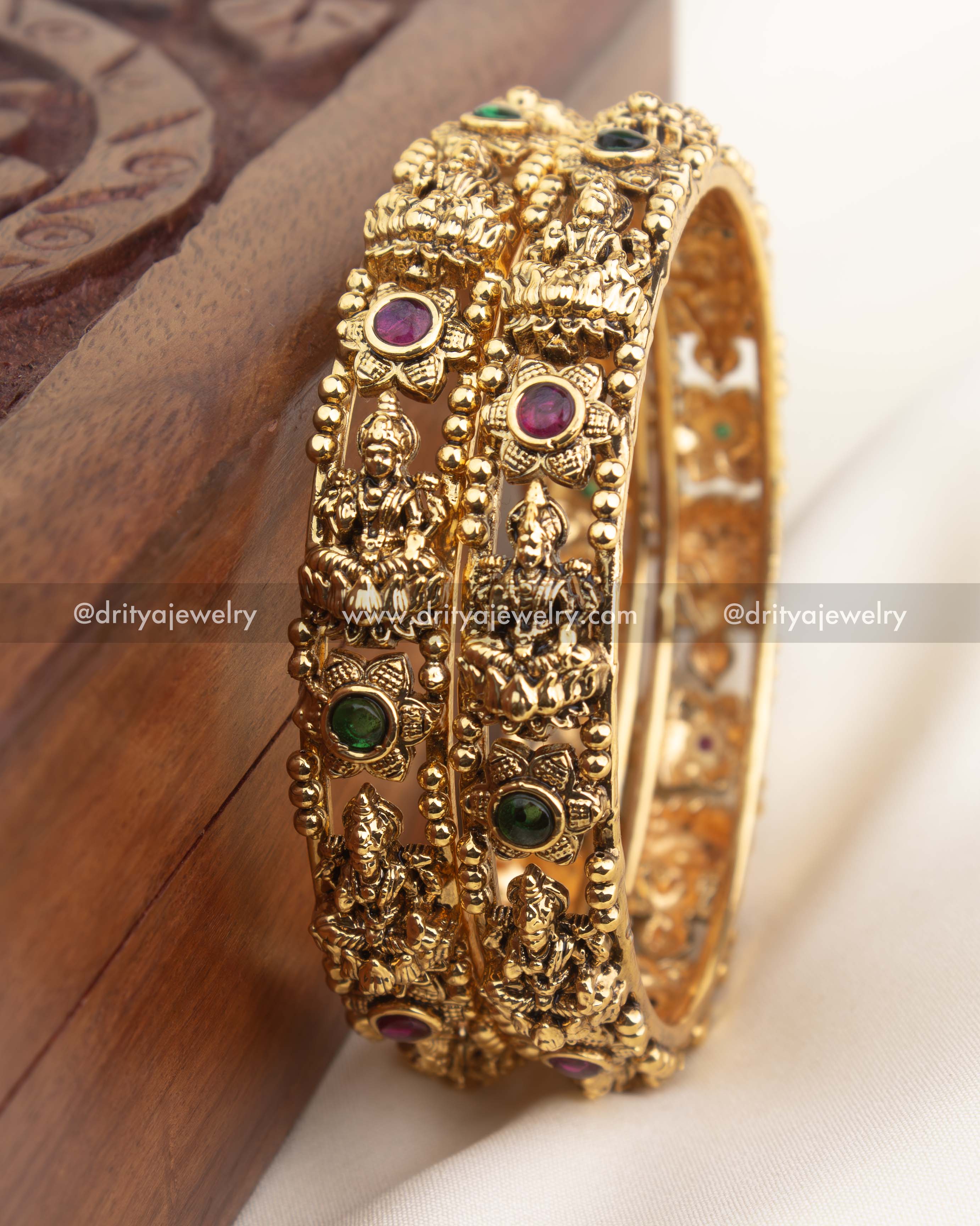 Detailed close-up of temple bangles with goddess engravings, beaded borders, and multicolor stone accents in antique finish.