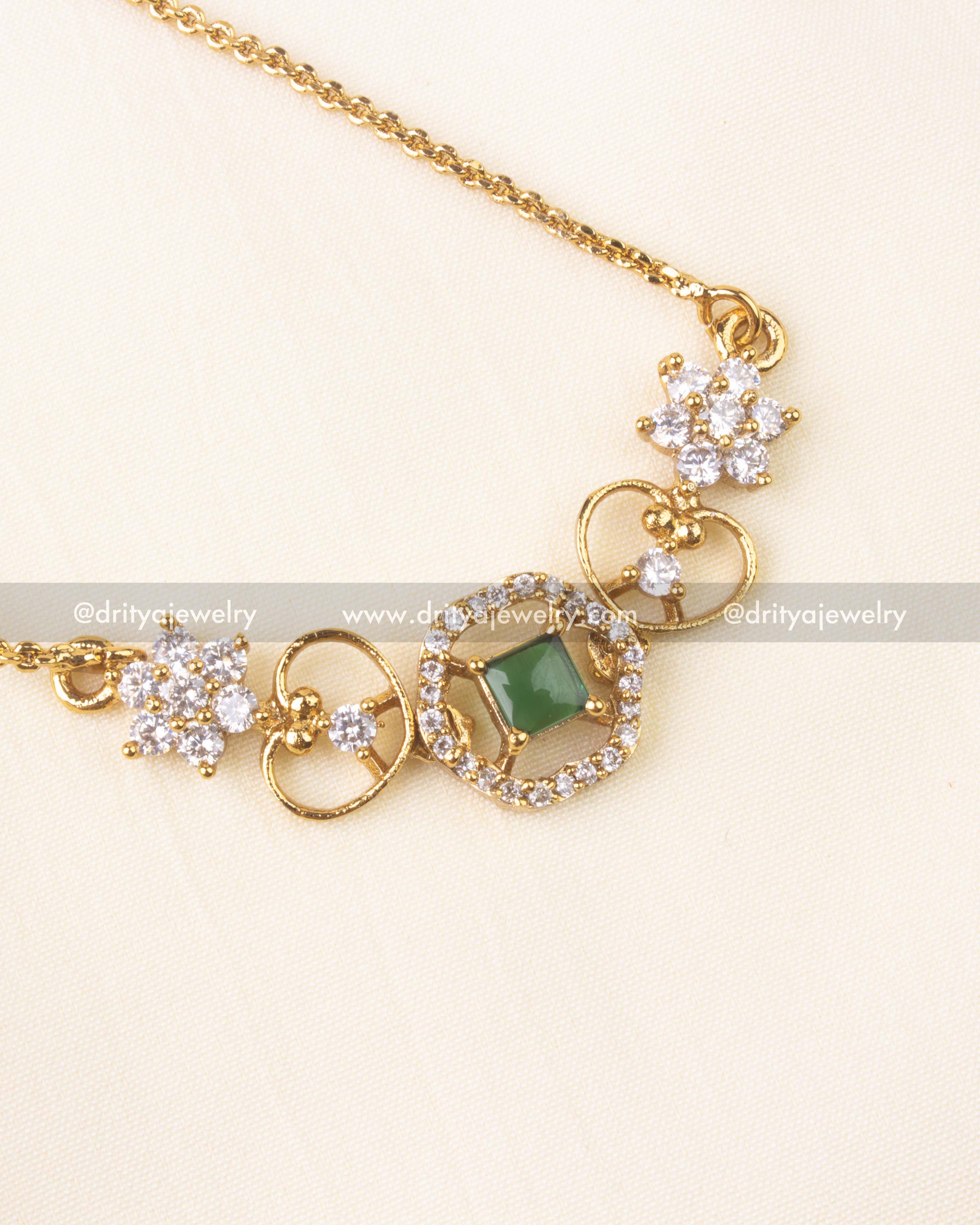 Square-cut emerald green stone surrounded by CZ detailing in a floral gold motif.