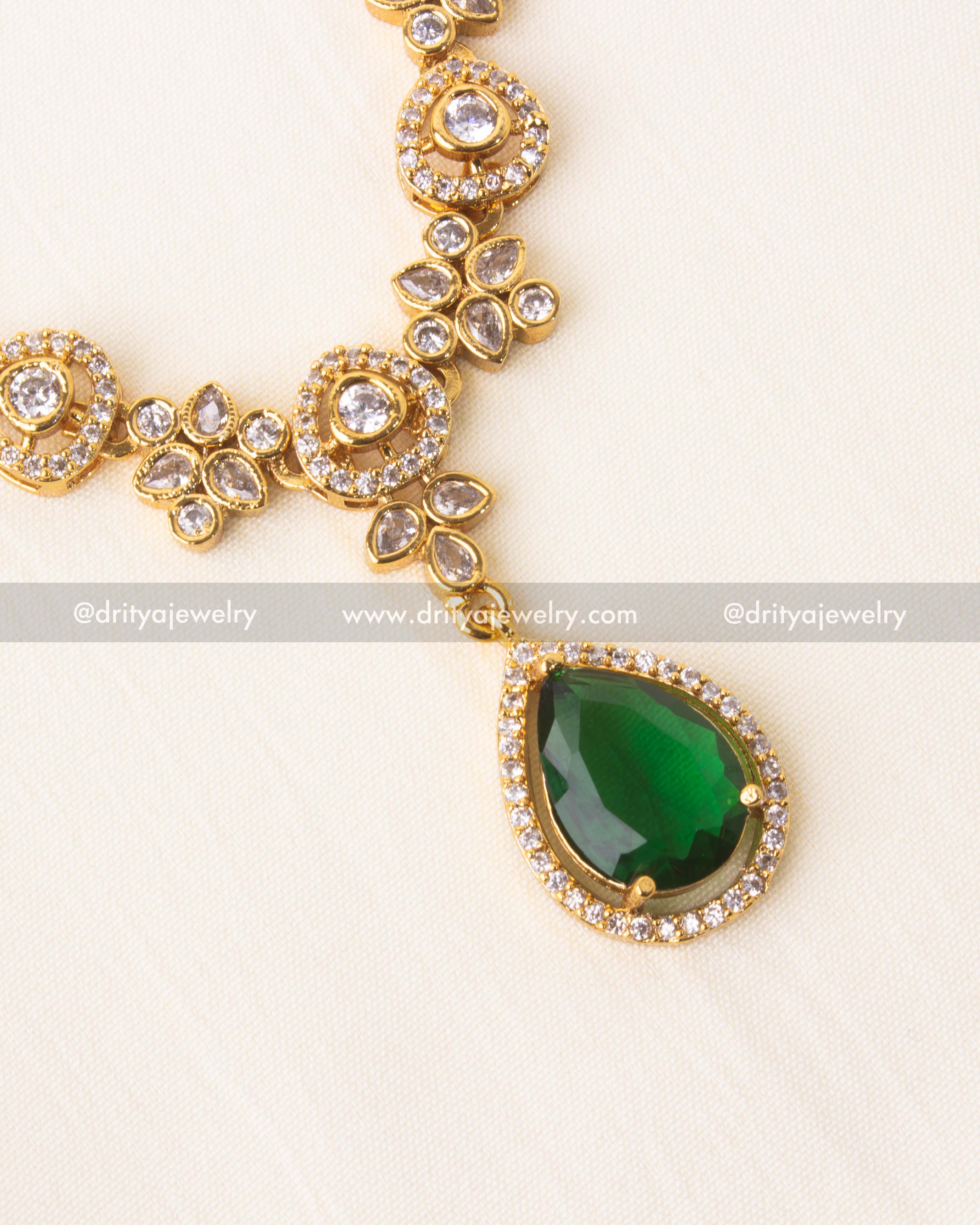 Detailed green teardrop pendant on floral stone-studded necklace.