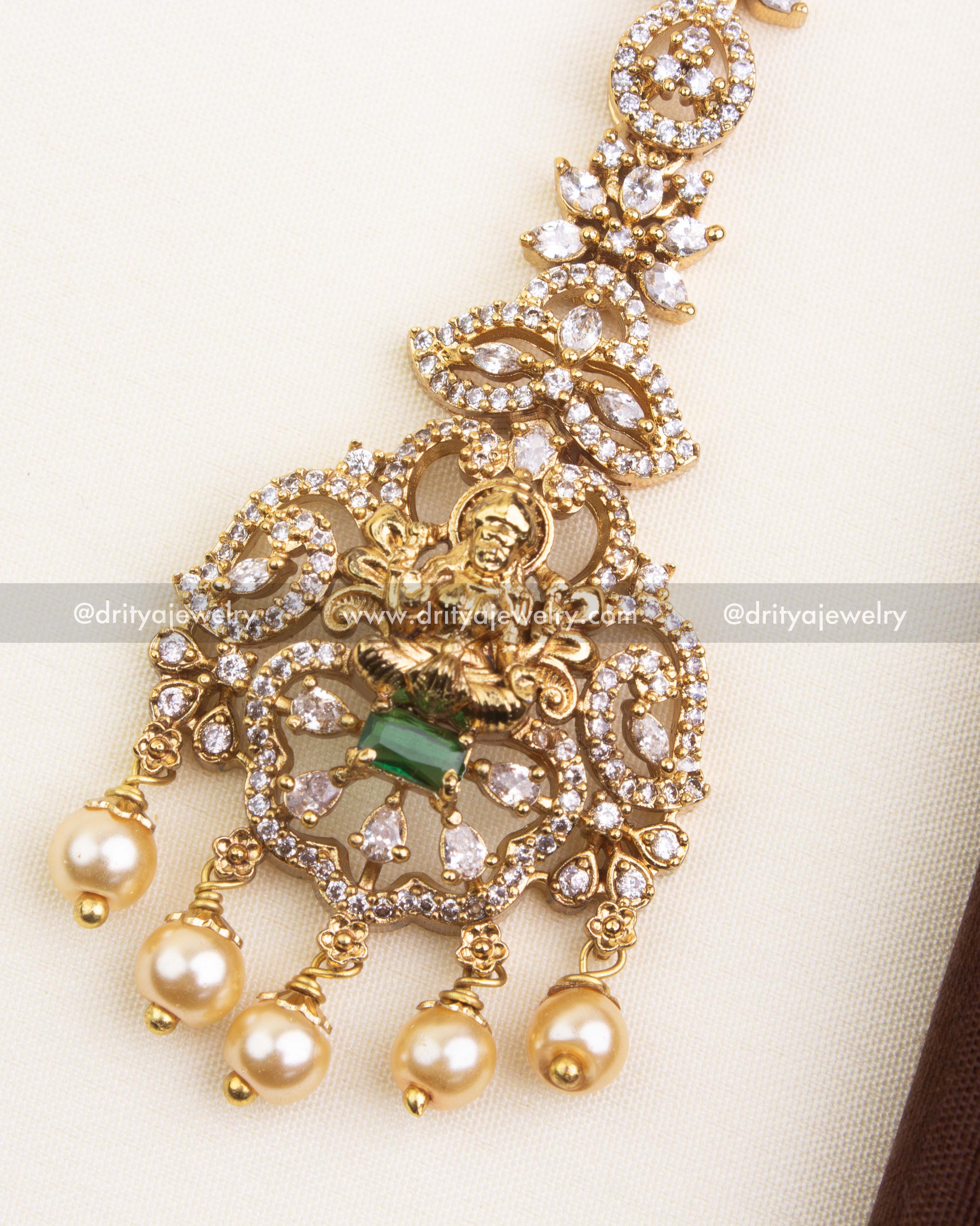 Detailed view of green maang tikka with goddess motif, CZ stones, and pearl danglers.