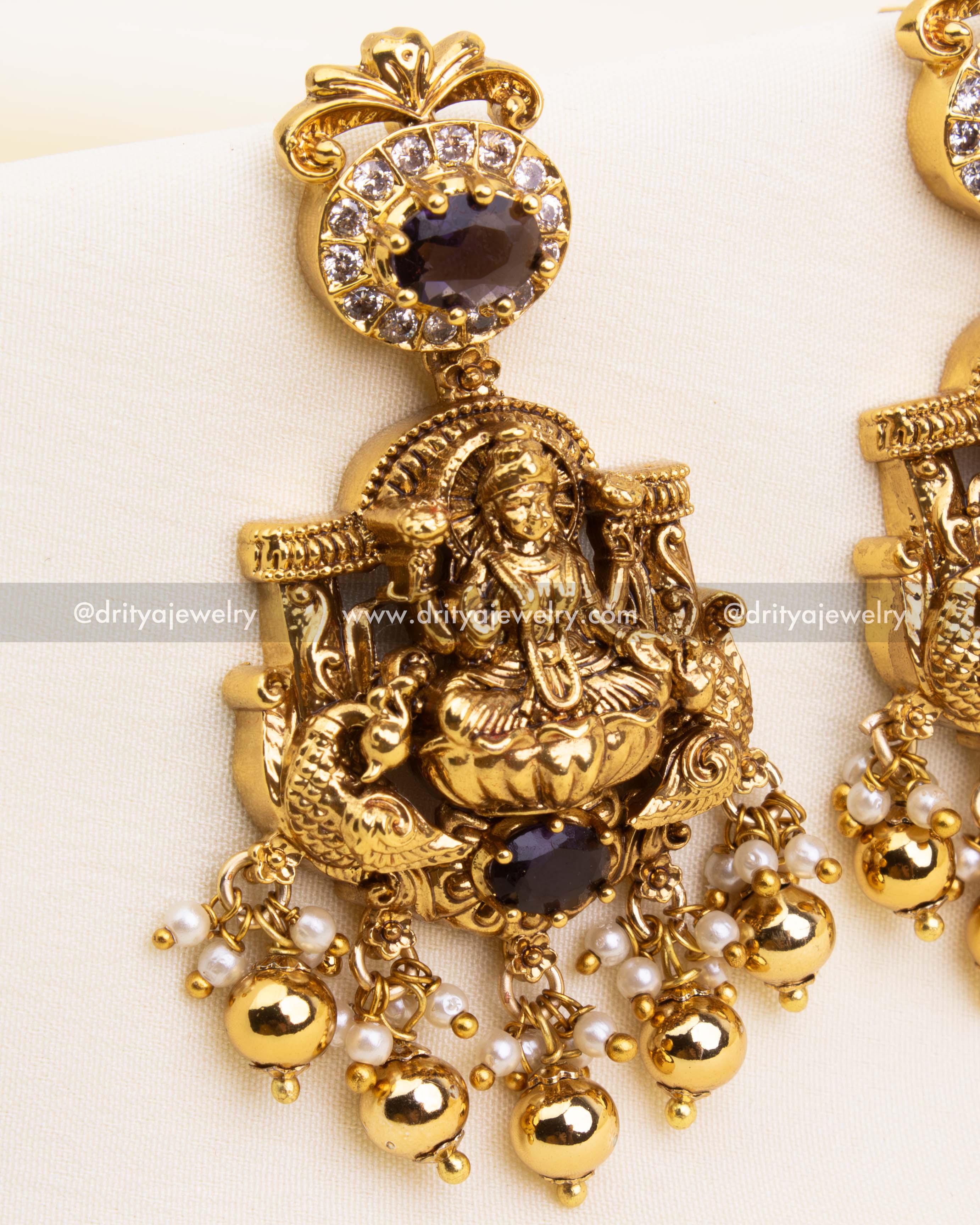 Zoomed-in view of traditional earrings with goddess Lakshmi detailing, purple stone setting, and white CZ embellishments