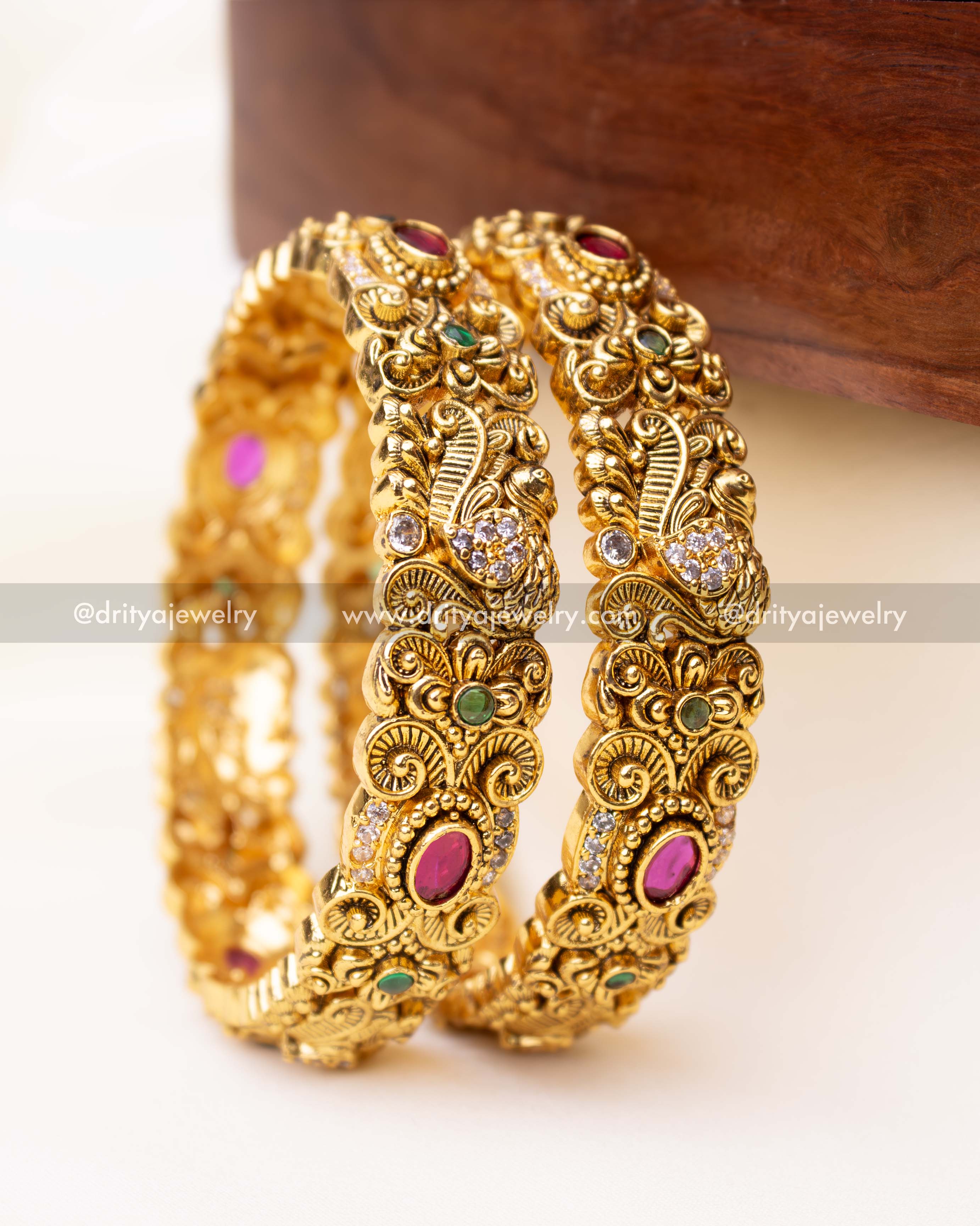 Pair of antique gold-finished Nakshi bangles adorned with ruby-red and emerald-green stones.