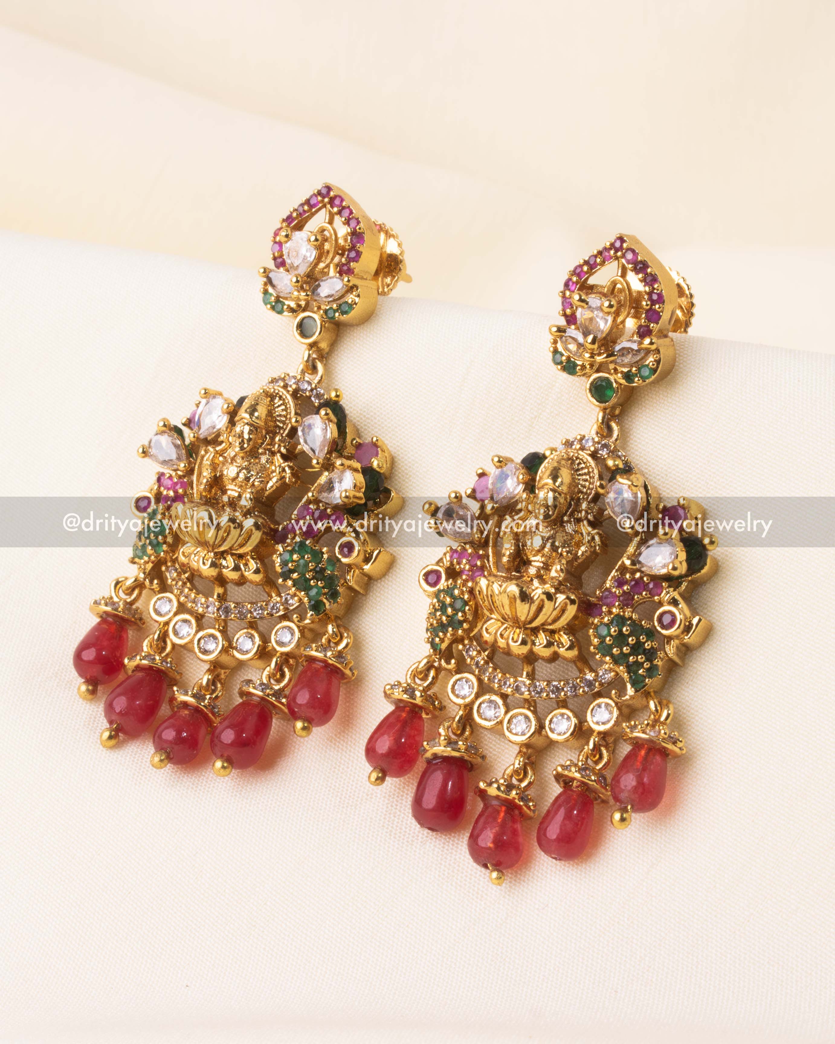 Detailed view of Nakshi-style earrings with intricate deity design and red bead clusters.