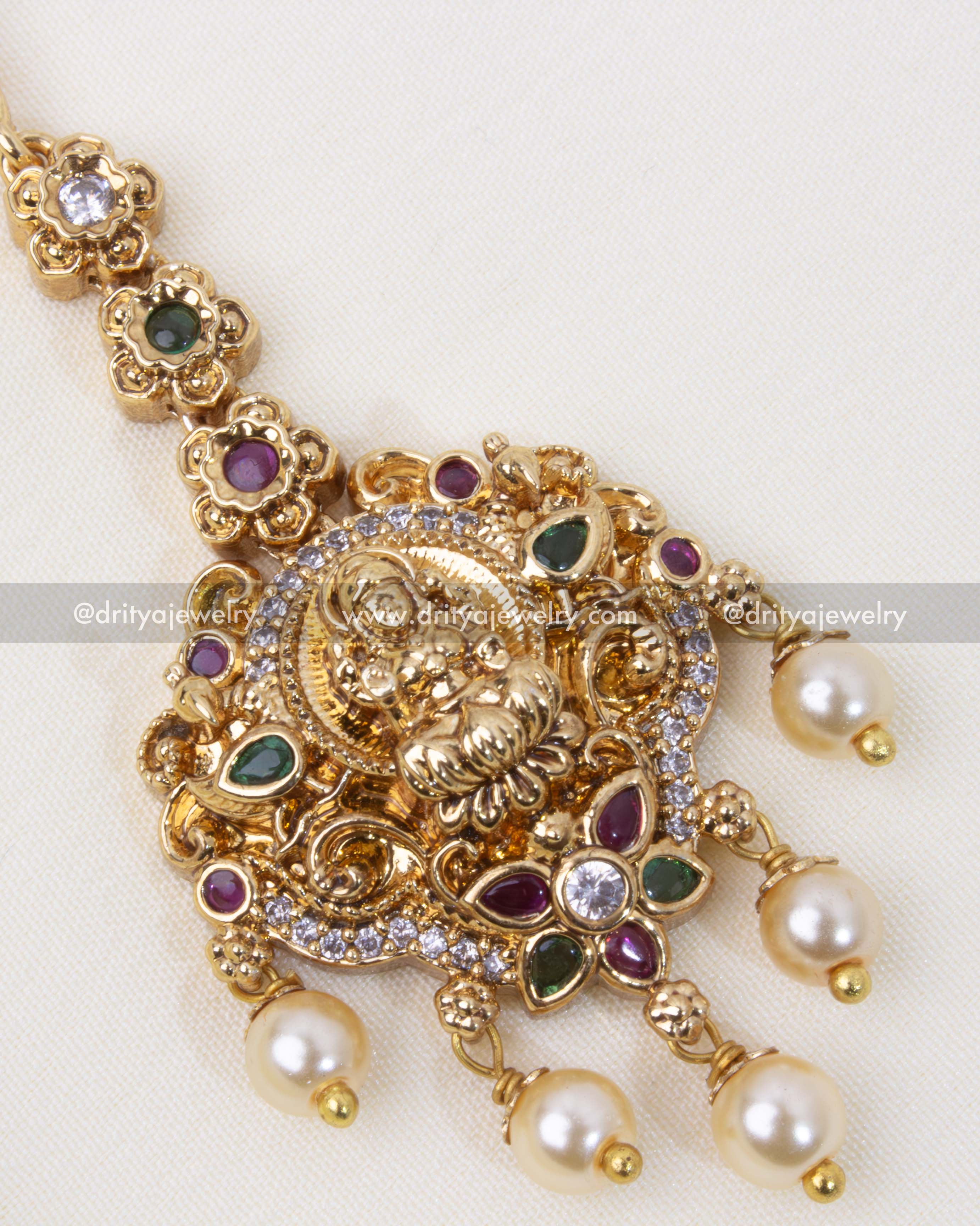 Intricately designed Nakshi Maang Tikka with an antique gold polish, Lakshmi motif, and pearl dangles for a traditional Indian look.