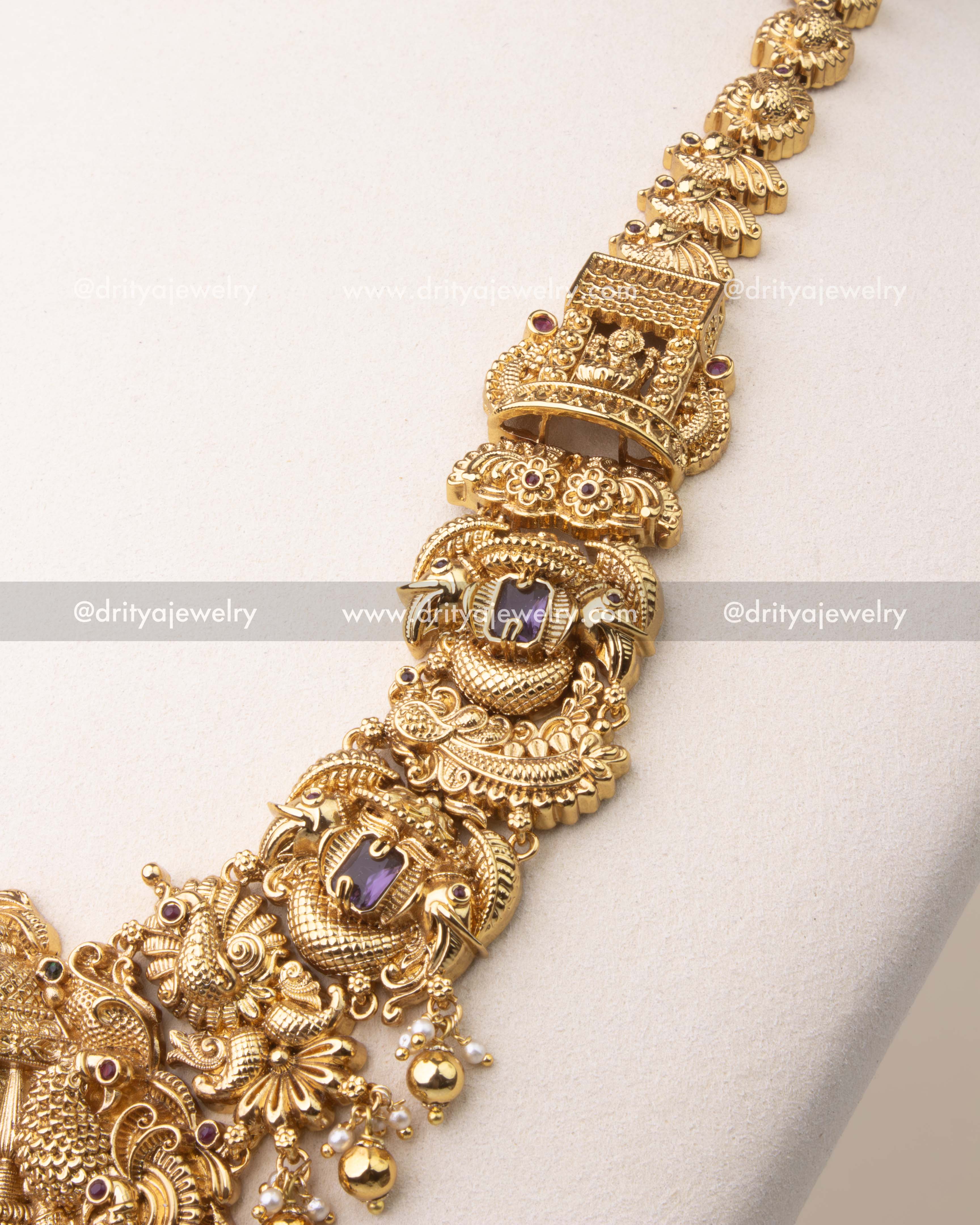 Intricate nakshi carvings with peacock motifs and violet stones on temple necklace chain.