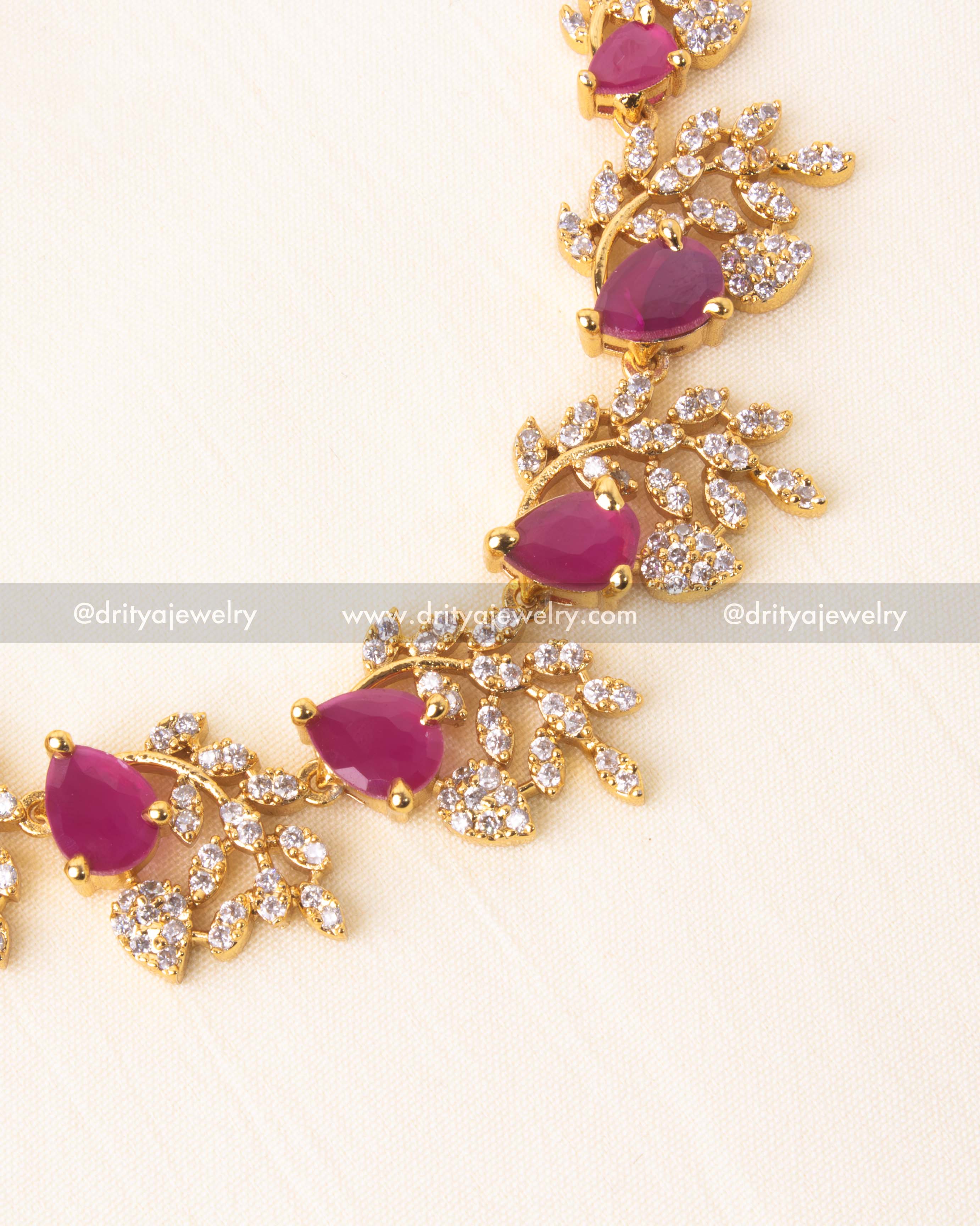 Close view of crystal leaf motifs and pink stones on gold-plated necklace.