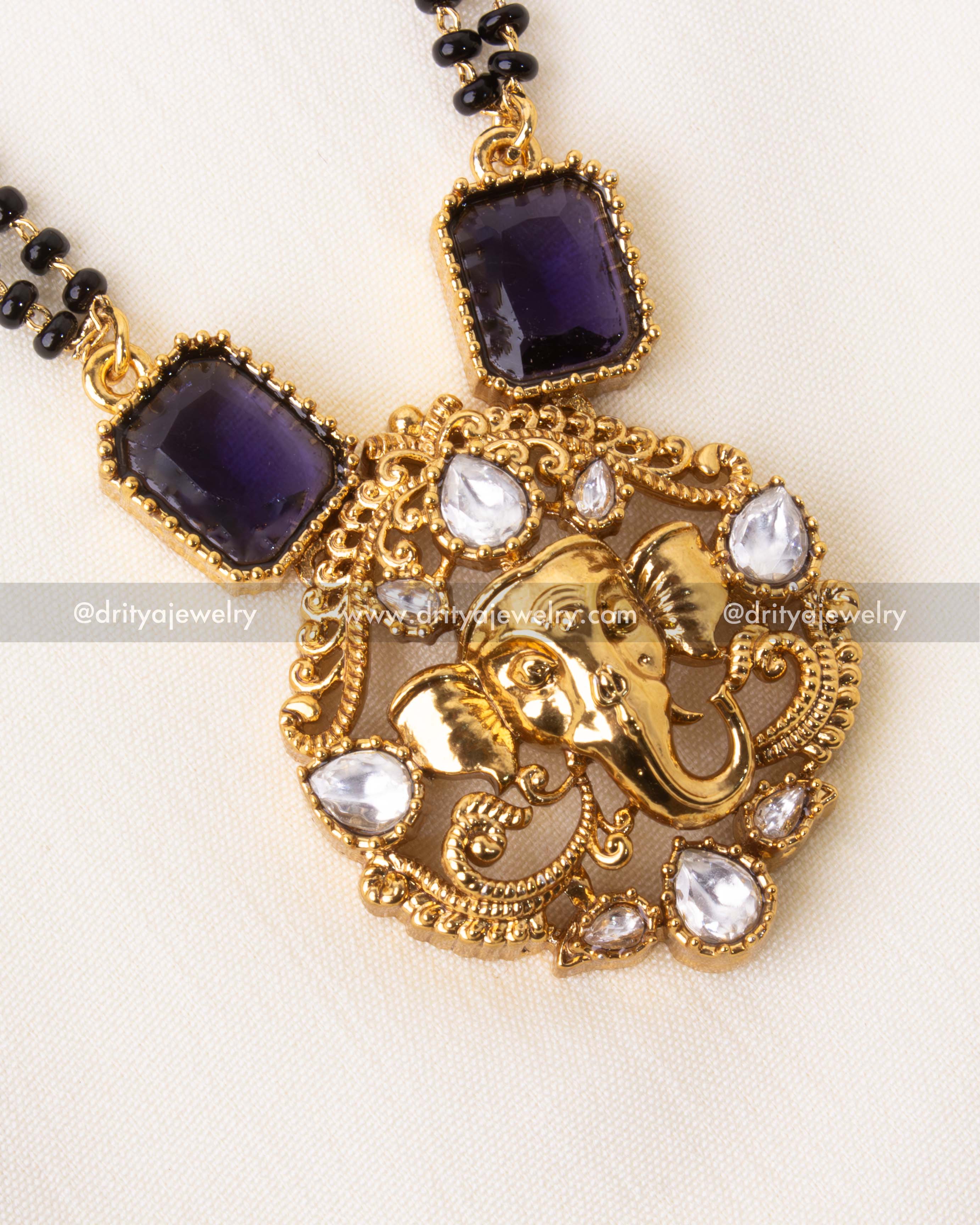 Detailed view of gold Ganesha pendant with purple stones and sparkling white accents.