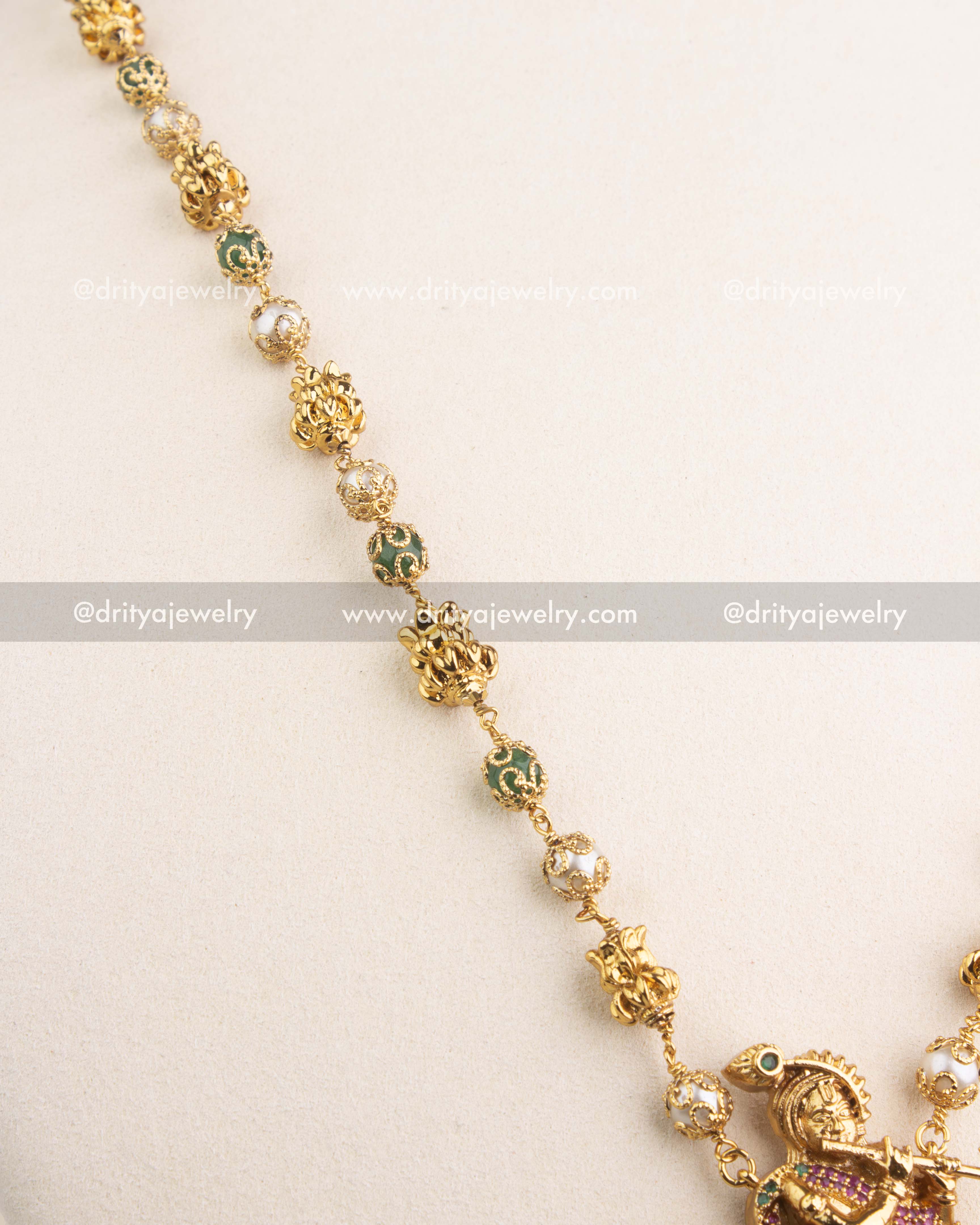 Detailed view of gold-finished chain with green enamel beads and pearl accents.