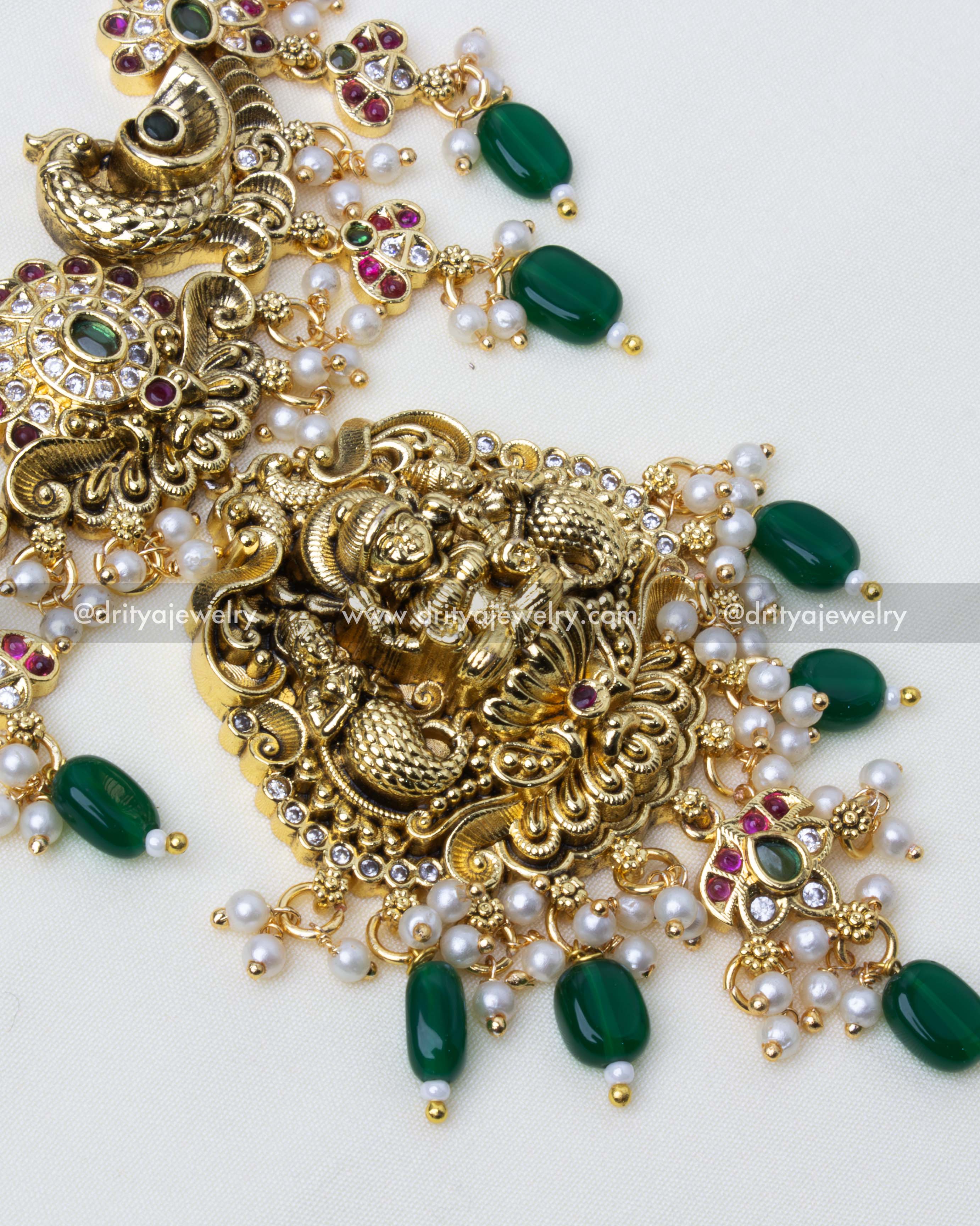 Close-up view of antique gold temple necklace featuring intricate deity and peacock motifs with green accents.