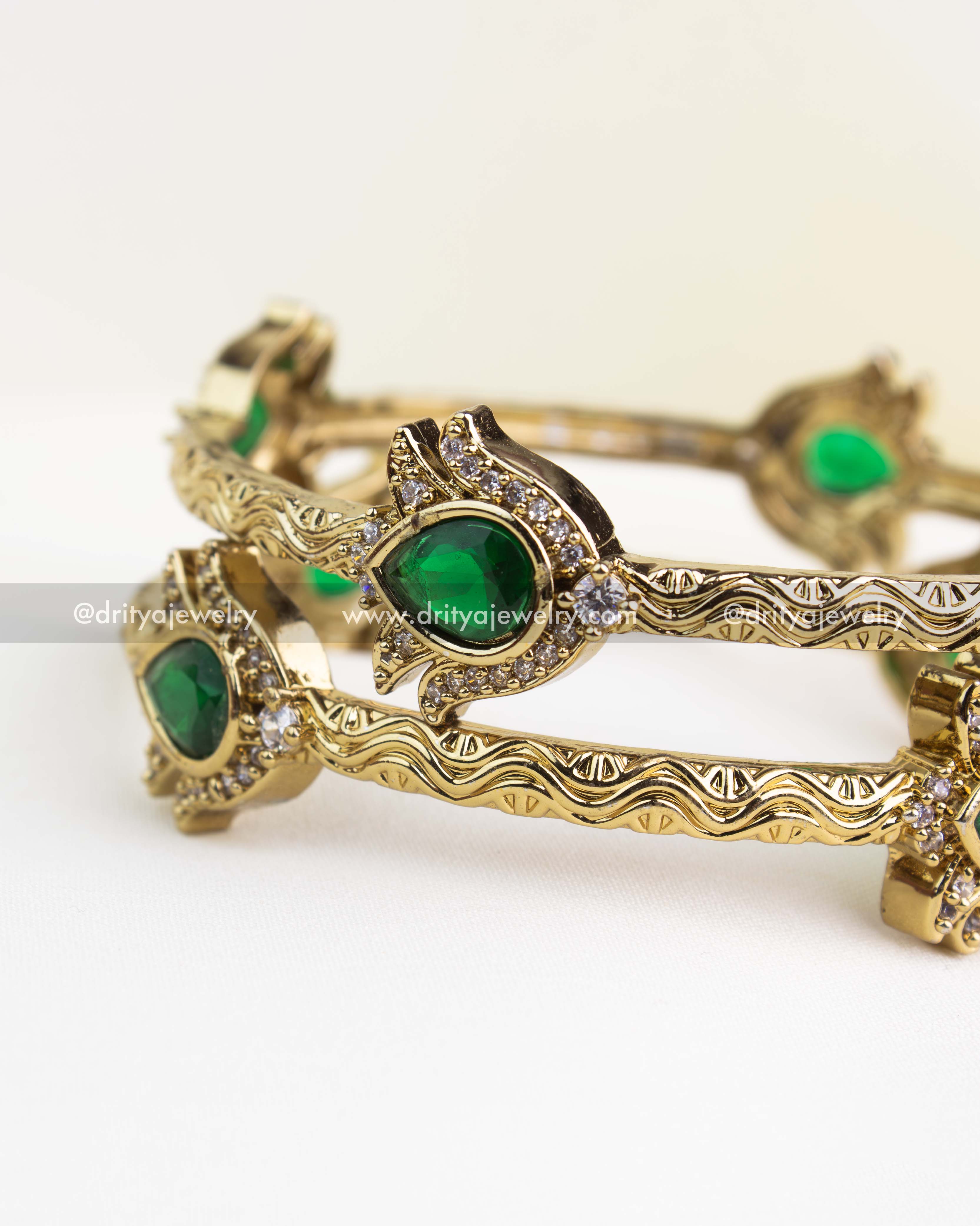 Intricate antique gold kada design with emerald green stone centerpiece and filigree engraving.