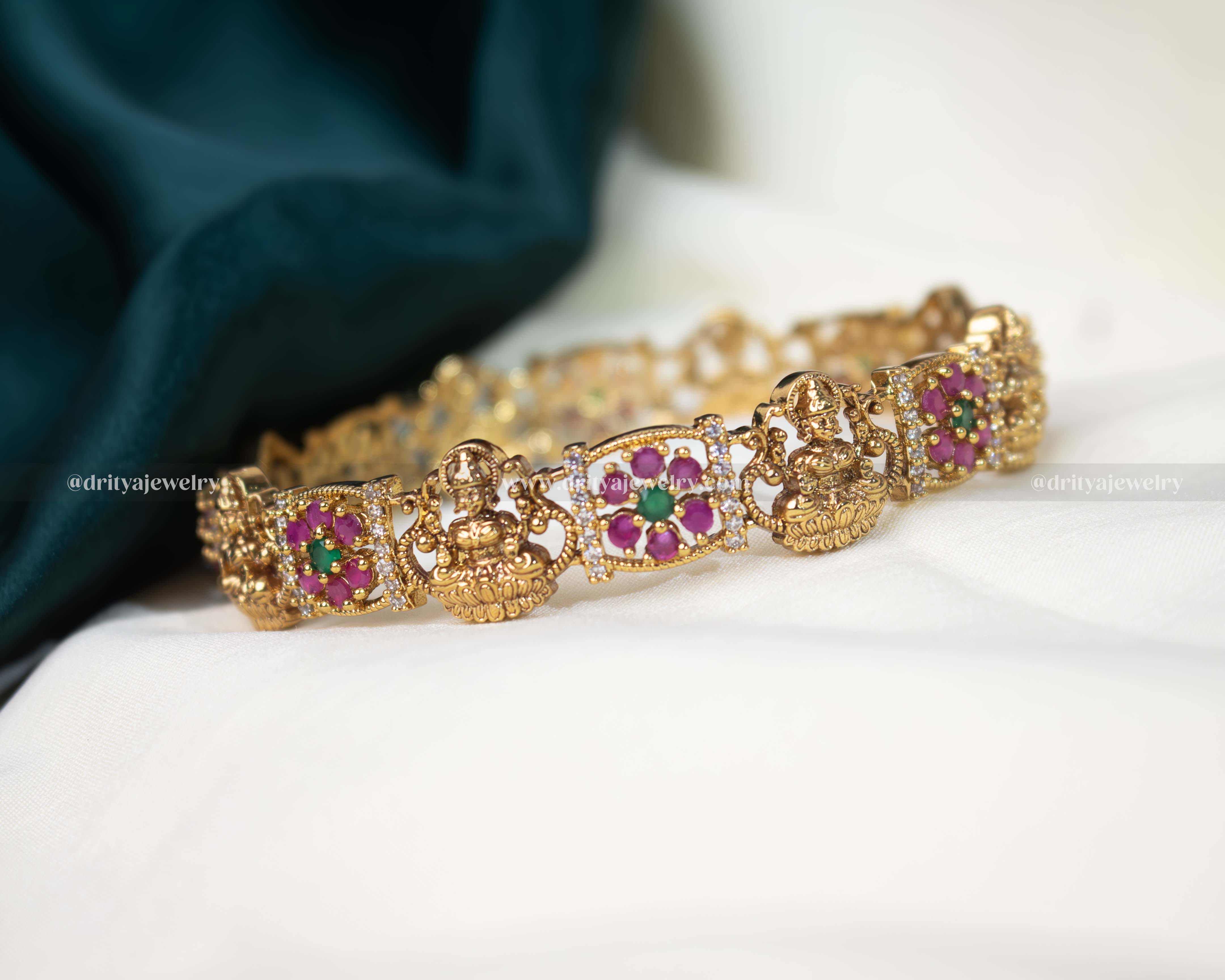Gold-tone Temple bangle with Lakshmi Devi motif and pink gemstone embellishments, perfect for traditional celebrations.