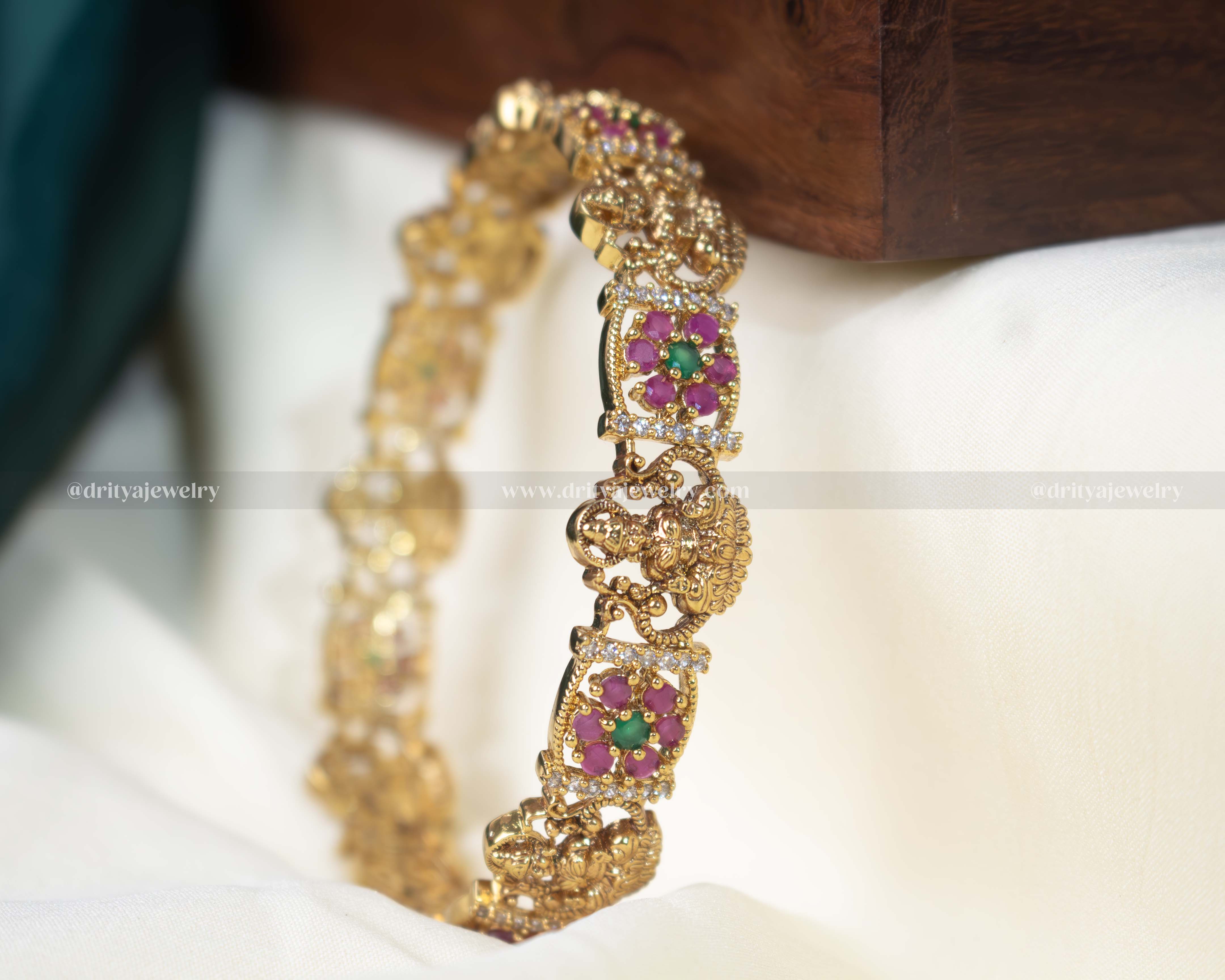 Gold-tone Temple bangle with Lakshmi Devi motif and pink gemstone embellishments, perfect for traditional celebrations.