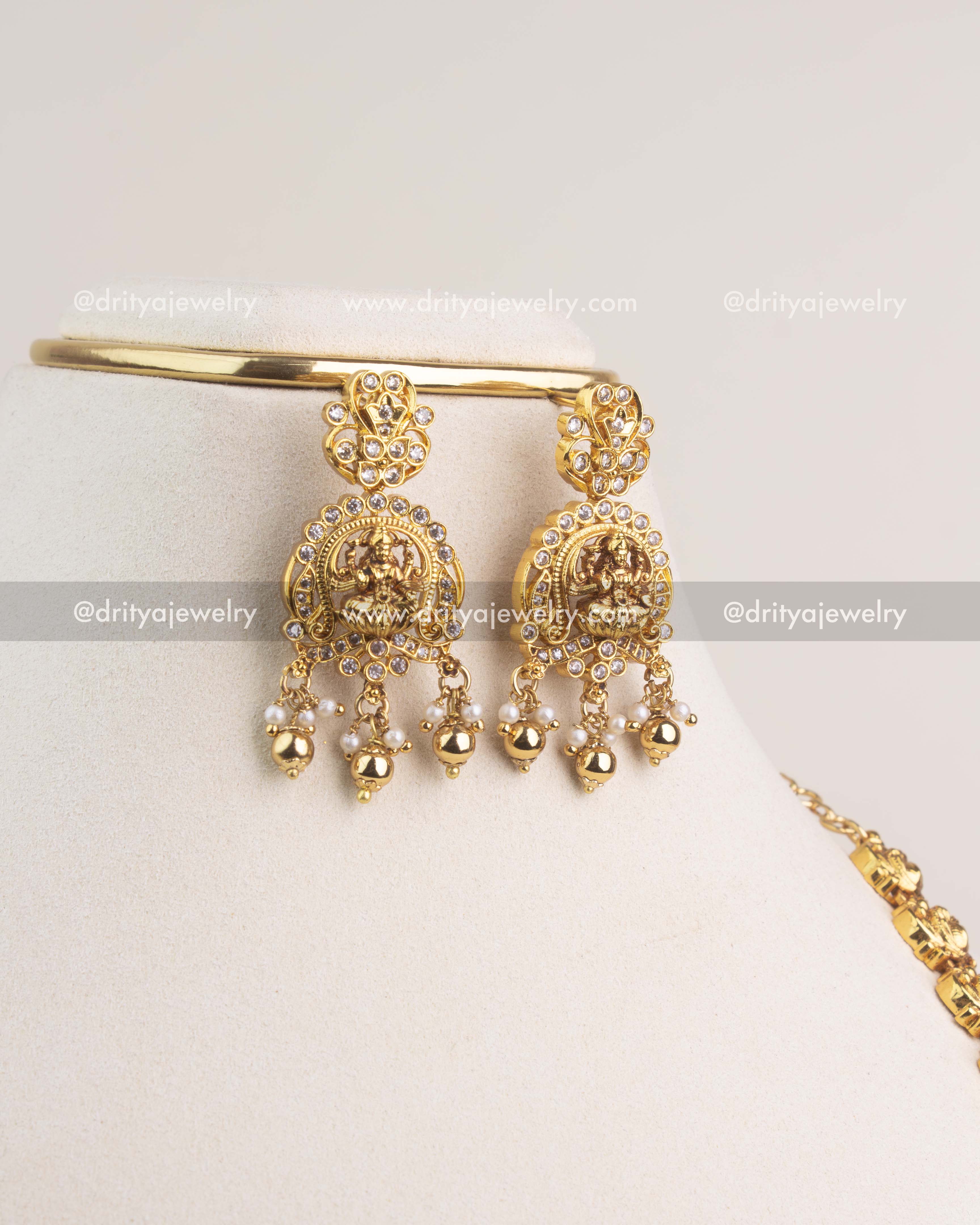 Temple-style Lakshmi Devi earrings with pearl and gold bead hangings in gold finish.