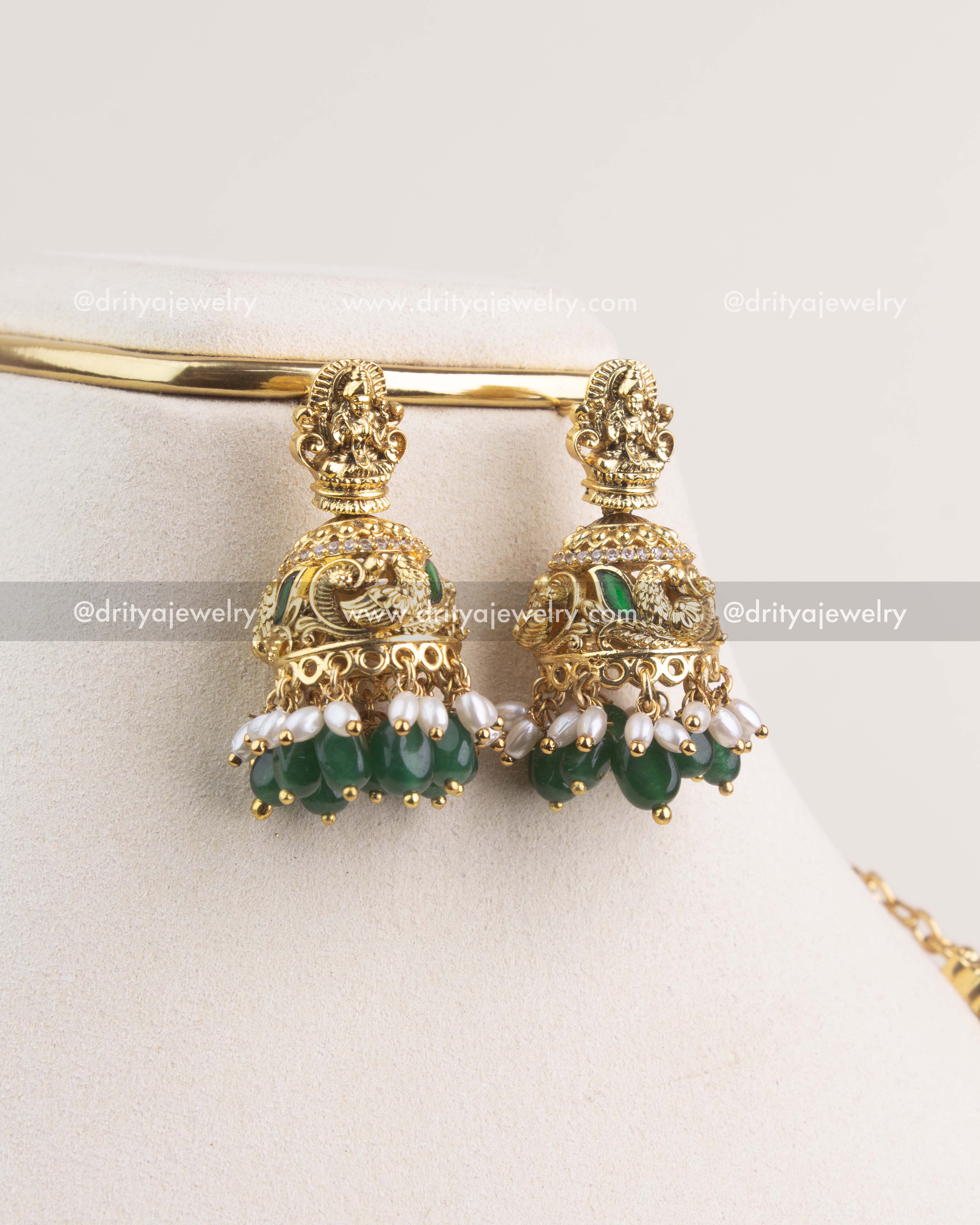 Gold jhumka earrings with Lakshmi motif, green beads, and pearl detailing.