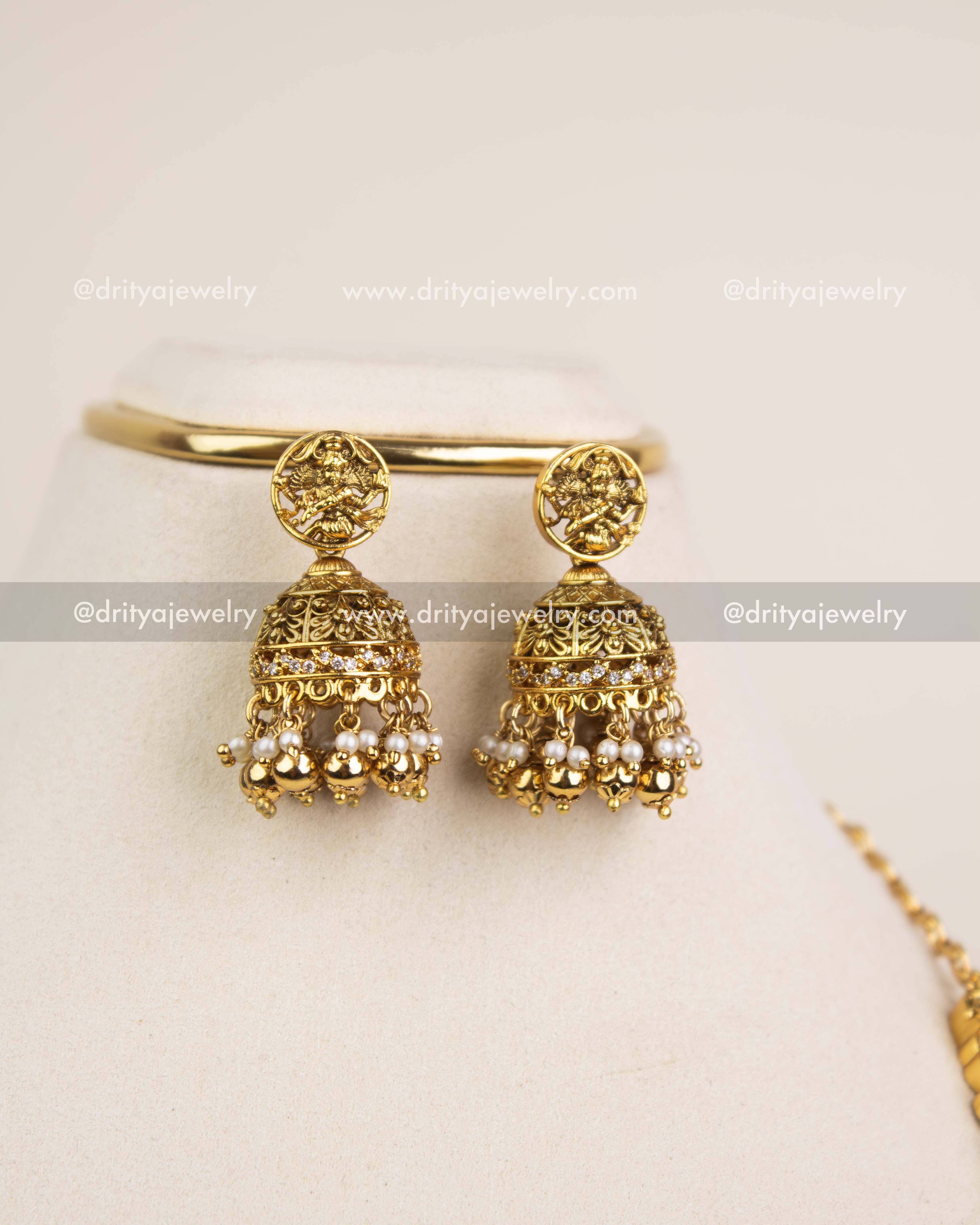 Premium antique gold jhumkas with deity motif and pearl hanging.