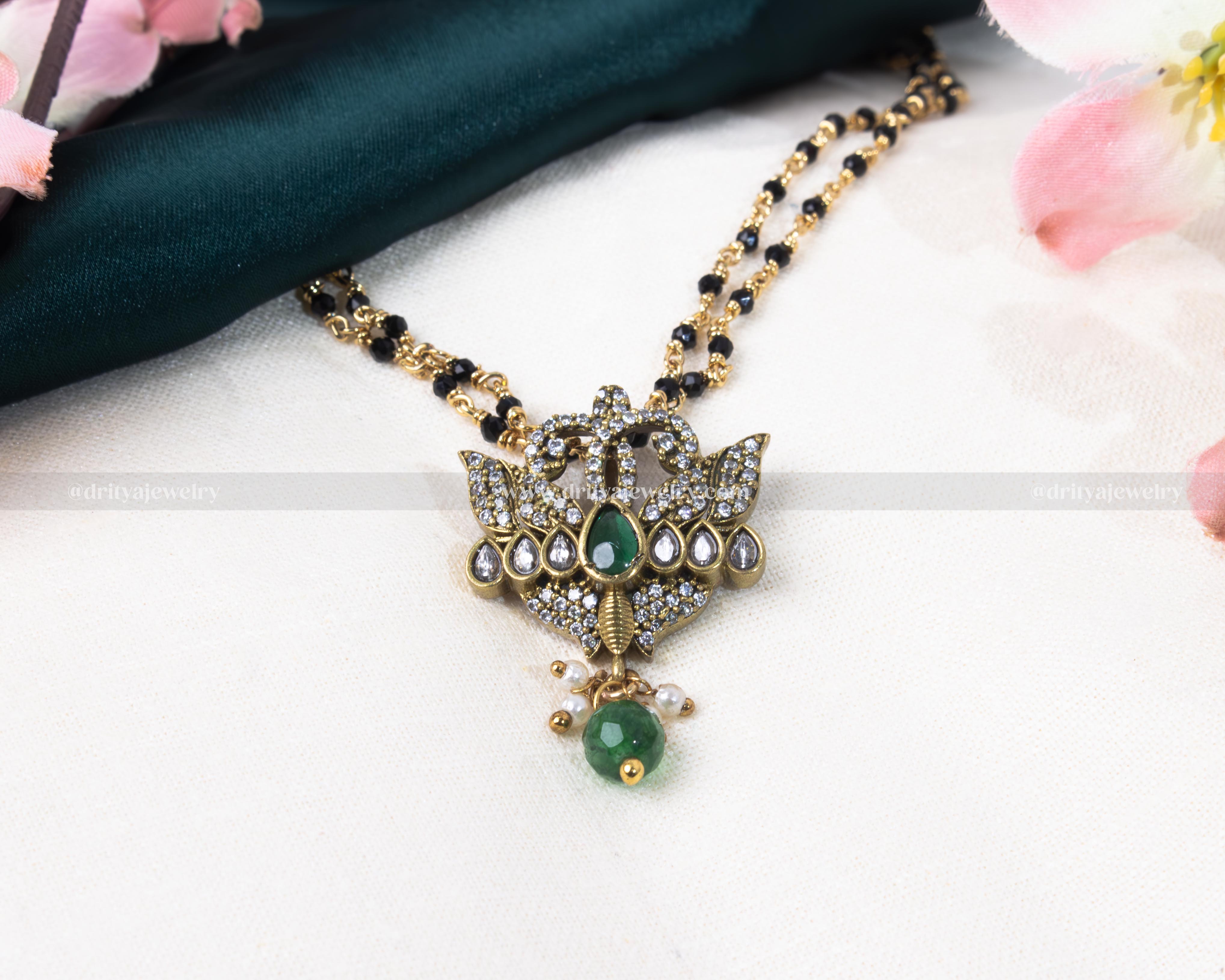 Luxurious black beads necklace featuring a gold-plated lotus-inspired pendant with green and red gemstone embellishments, blending tradition with modern elegance.