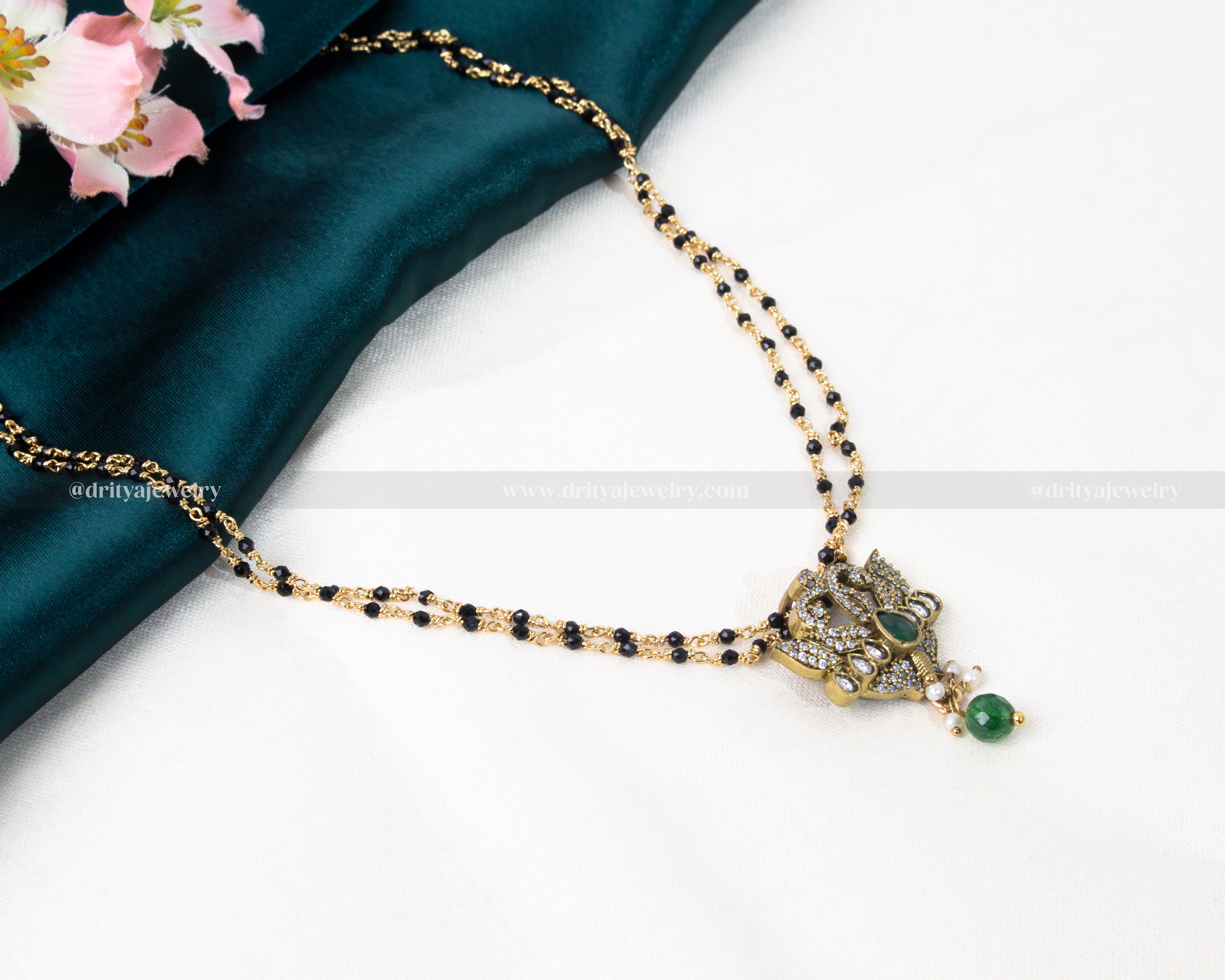 Luxurious black beads necklace featuring a gold-plated lotus-inspired pendant with green and red gemstone embellishments, blending tradition with modern elegance.