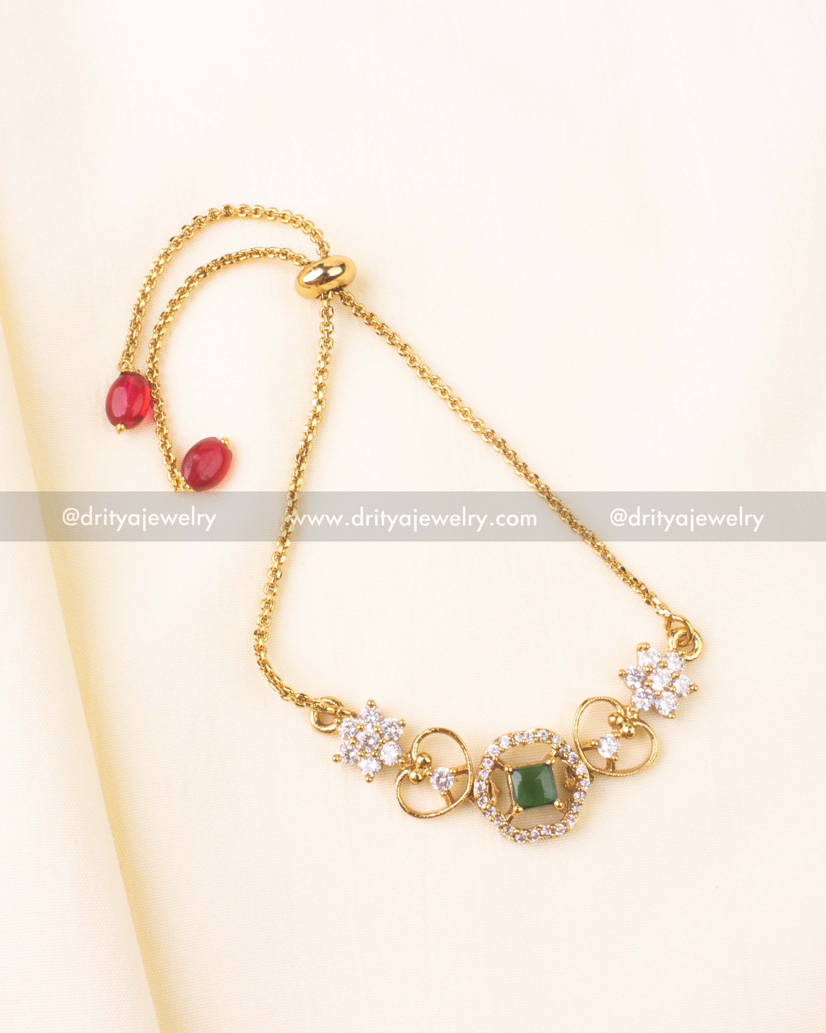 Square-cut emerald green stone surrounded by CZ detailing in a floral gold motif.