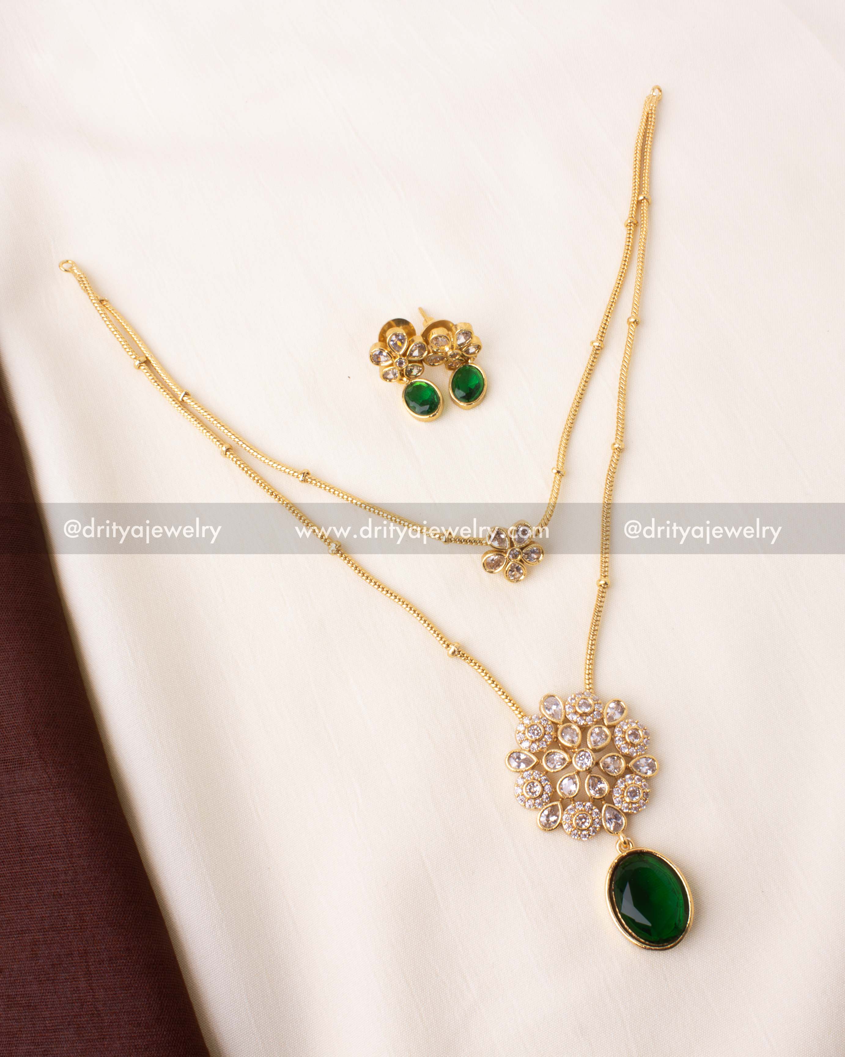 Double-layered necklace with kundan floral motif and emerald green pendant.