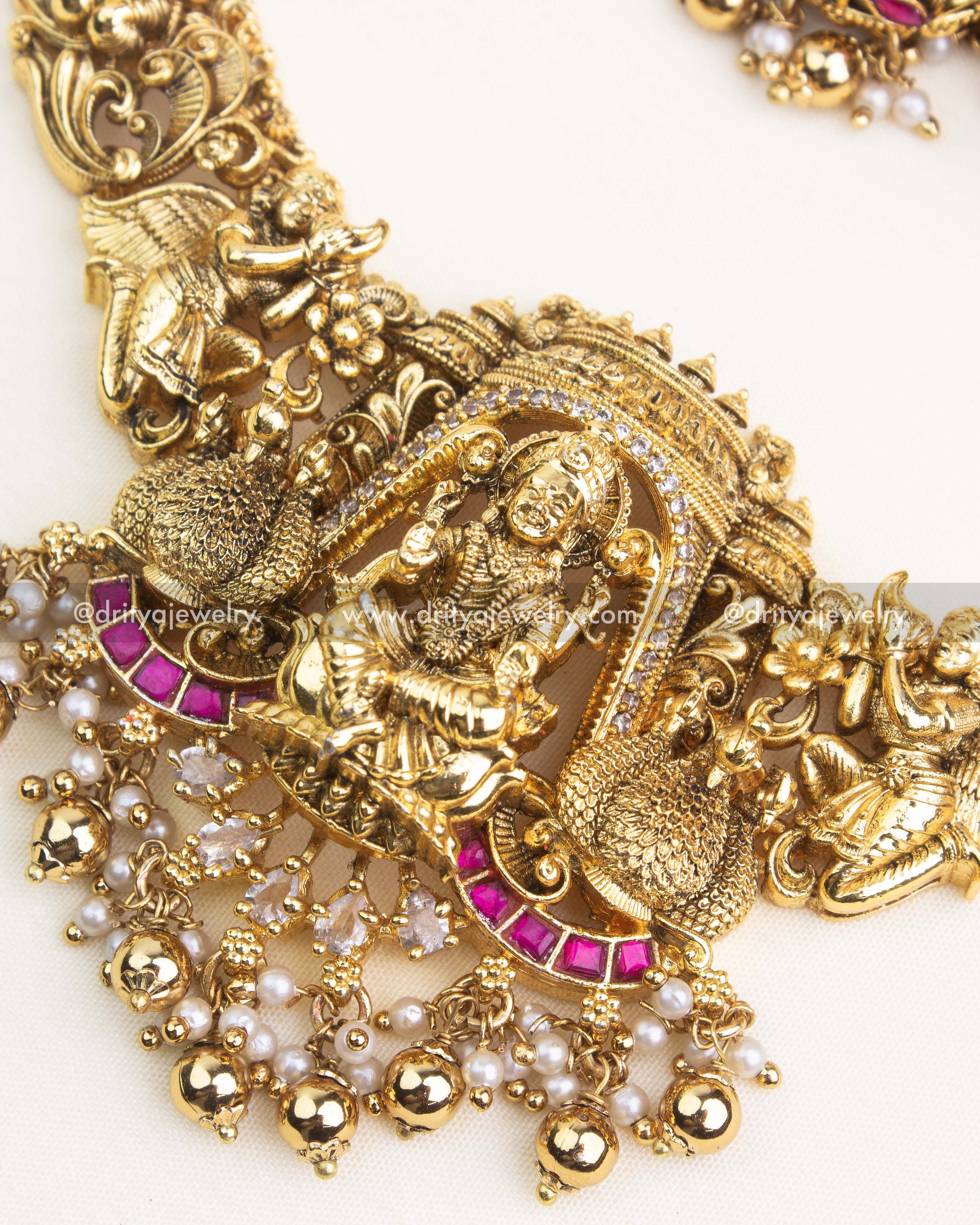 Close-up of temple necklace showing detailed Lakshmi pendant, peacock motifs, pearl hangings, and kemp stones.