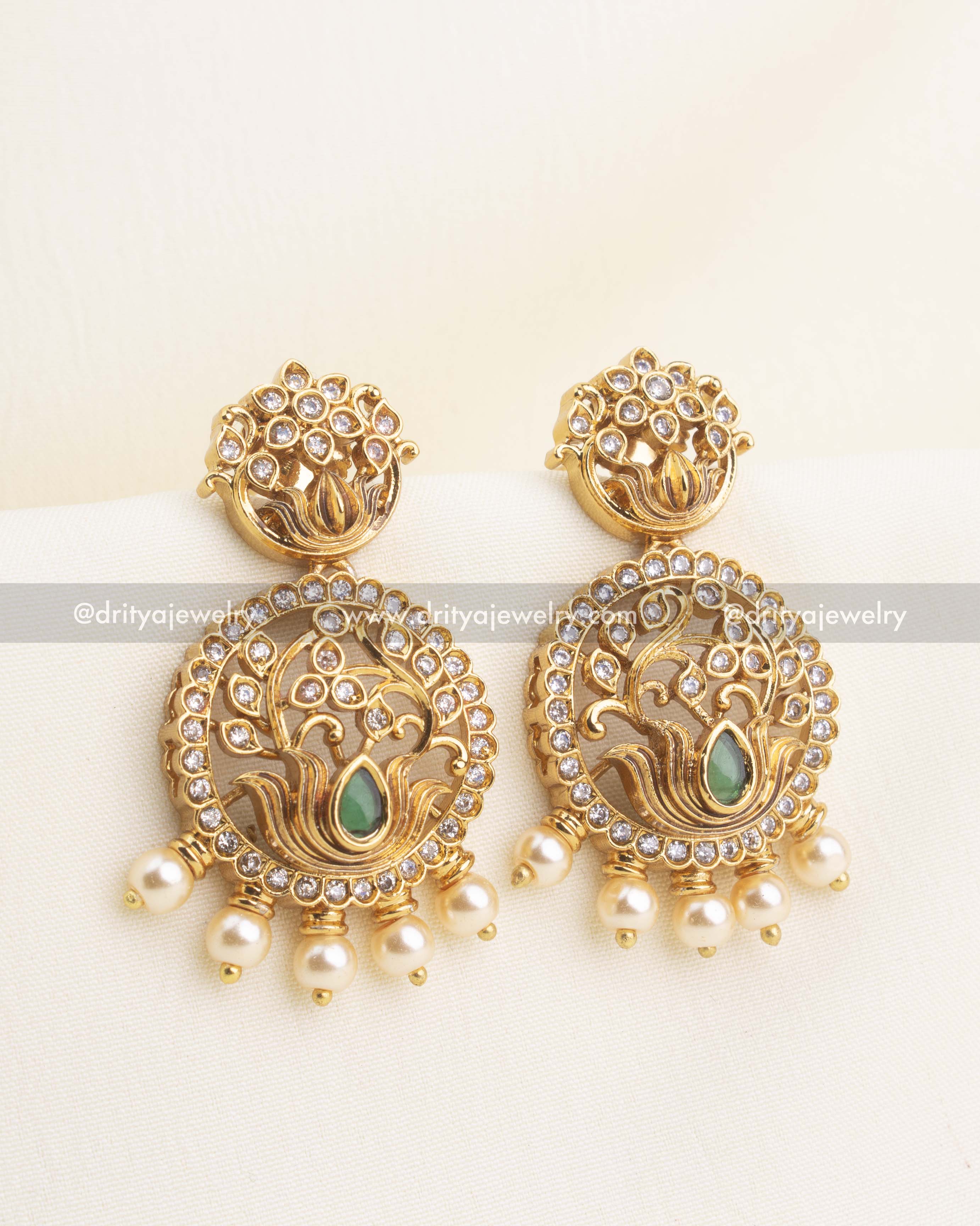 Gold lotus motif earrings with floral tops, CZ halo, green gemstone, and pearl droplets.