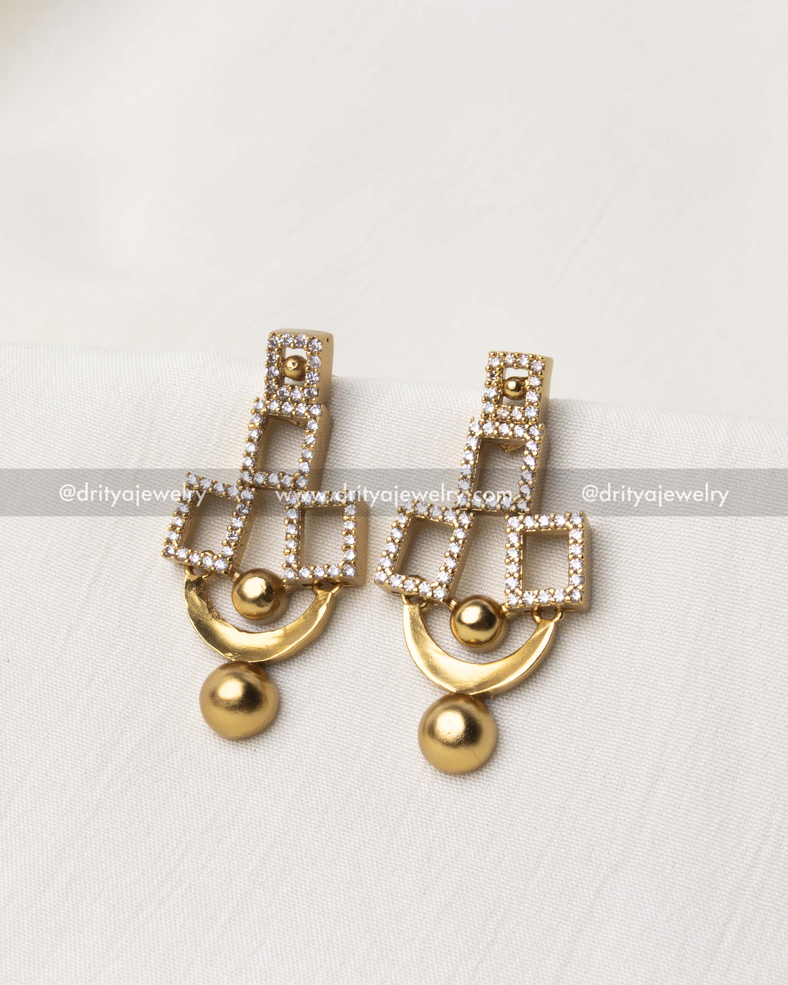 Close-up of geometric dangler earrings with cubic zirconia stones and a golden finish.