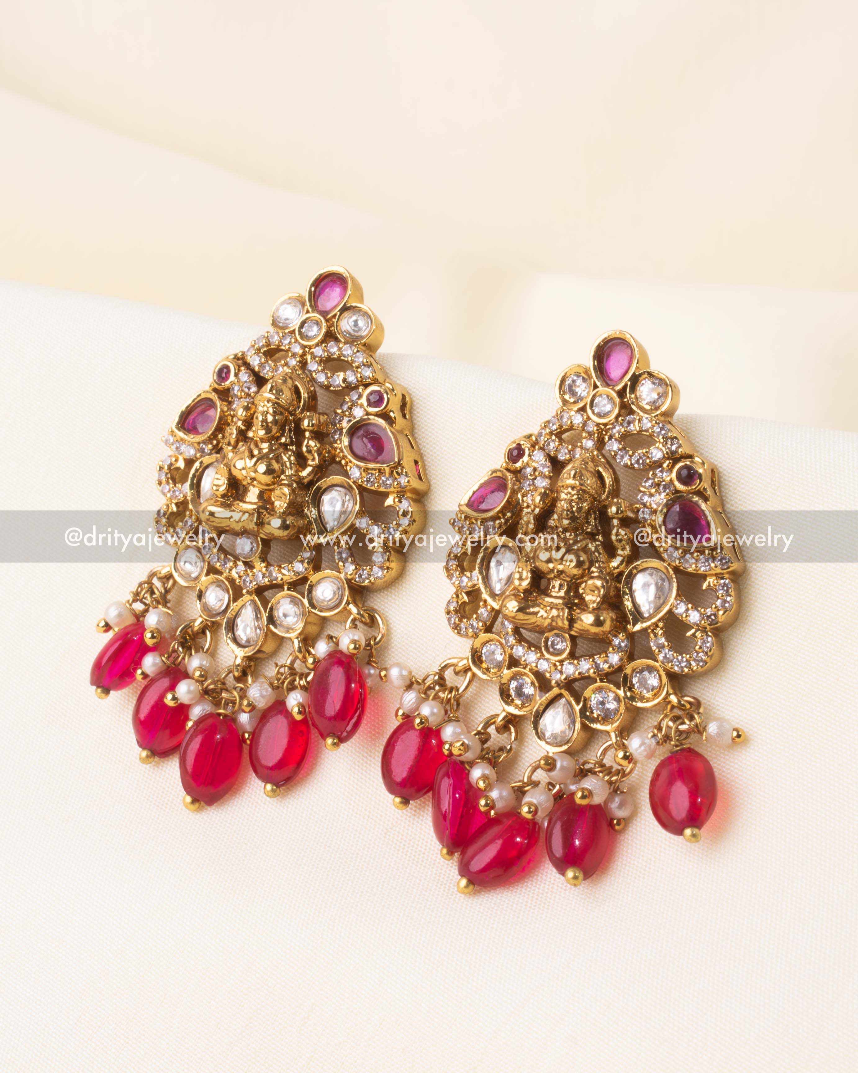 Gold-plated Lakshmi temple earrings with kundan embellishments and dangling red drops.