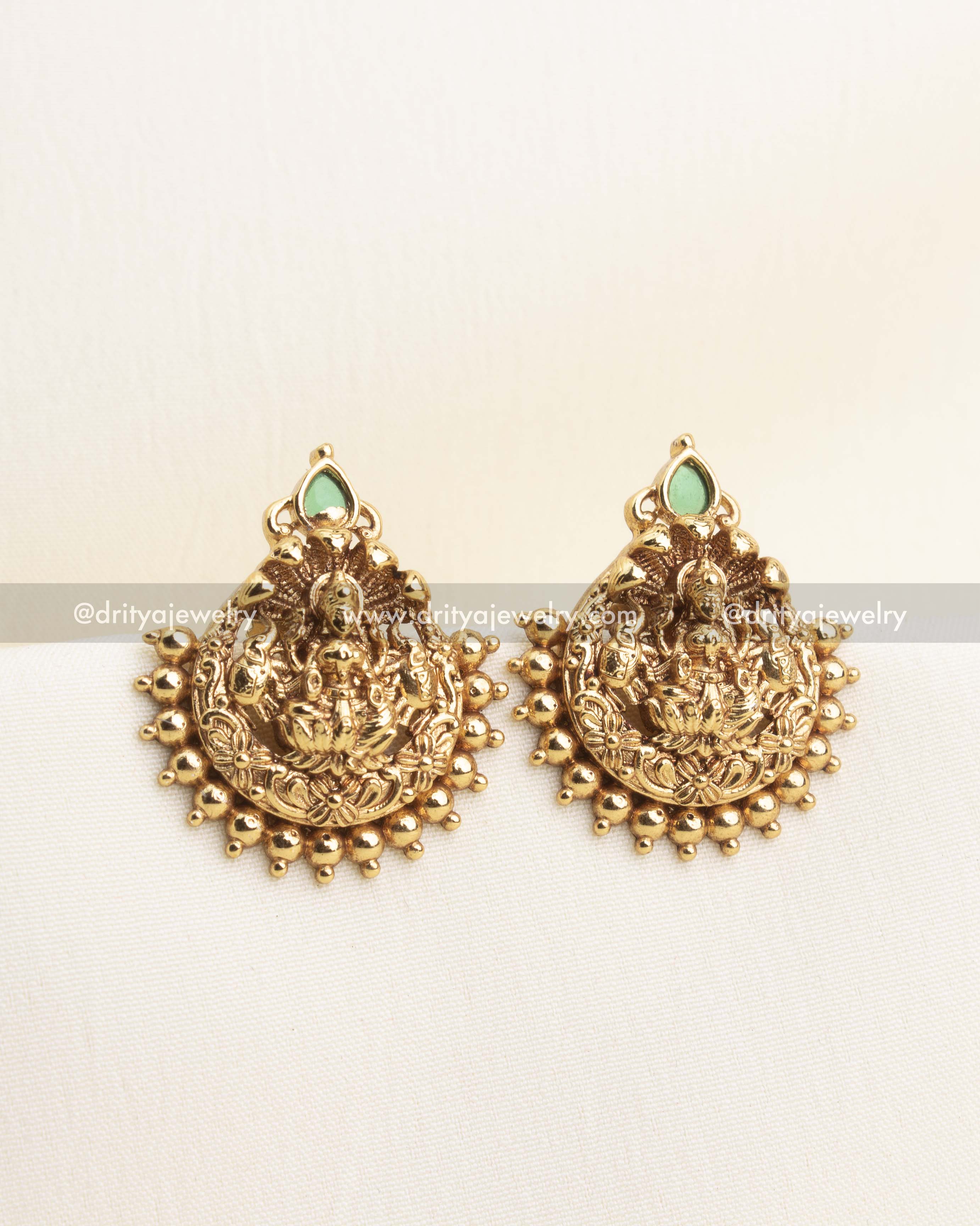 lose-up of antique gold Lakshmi pendant with bead clusters and green stone accent.
