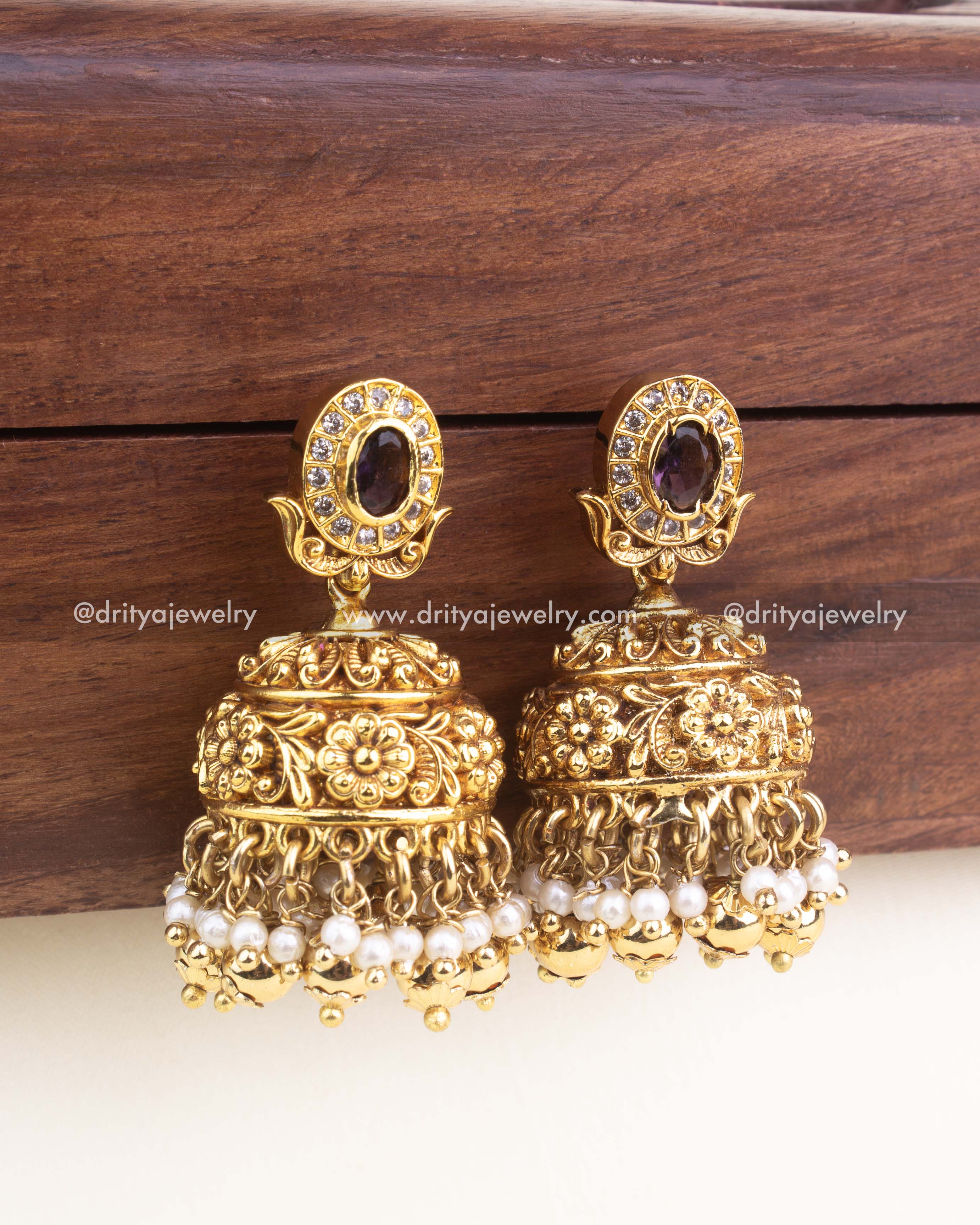 Antique gold jhumka earrings with embossed floral nakshi work, CZ stone top, and pearl clusters.