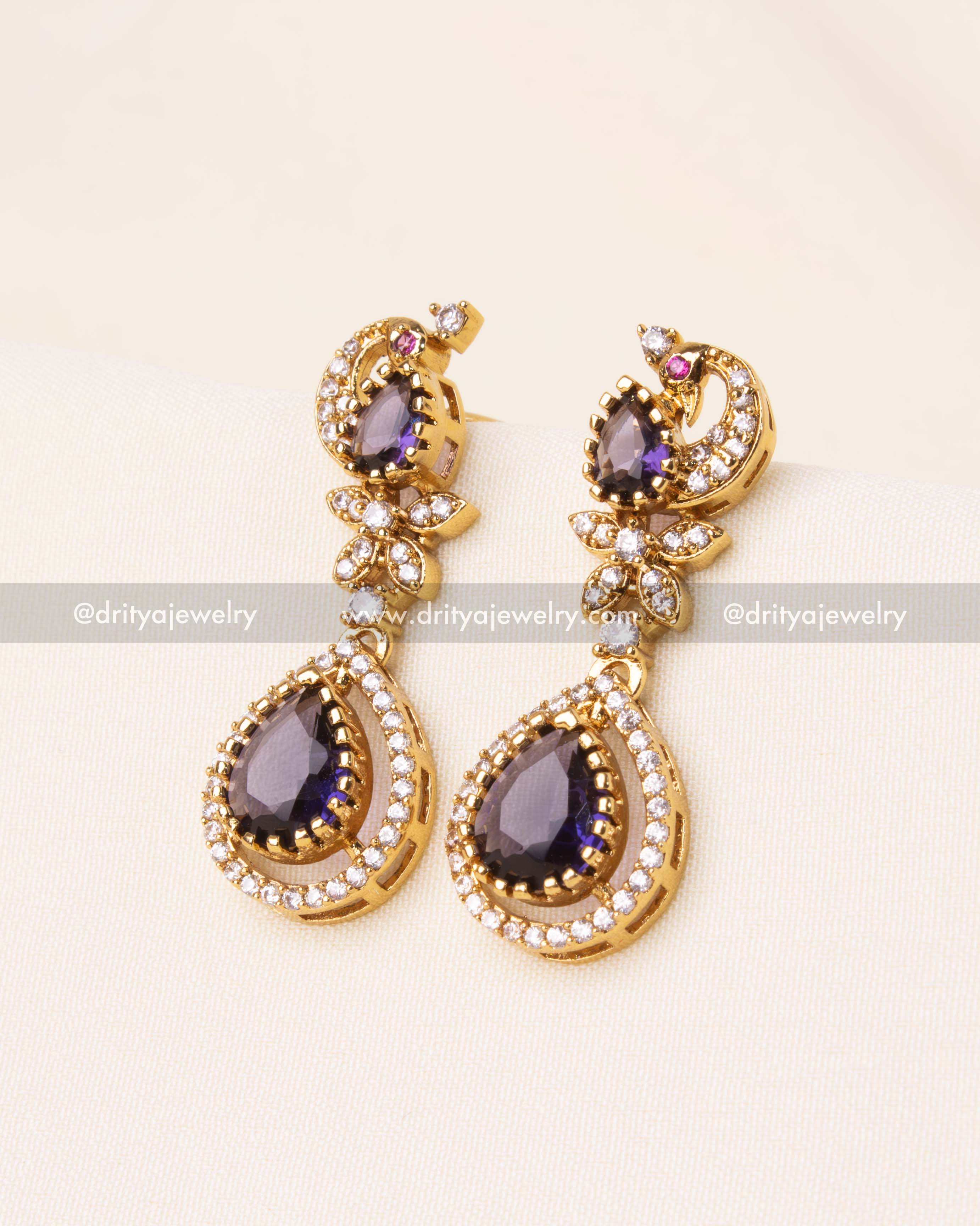 legant gold-plated peacock motif earrings with shimmering white stones and purple gemstone drops.