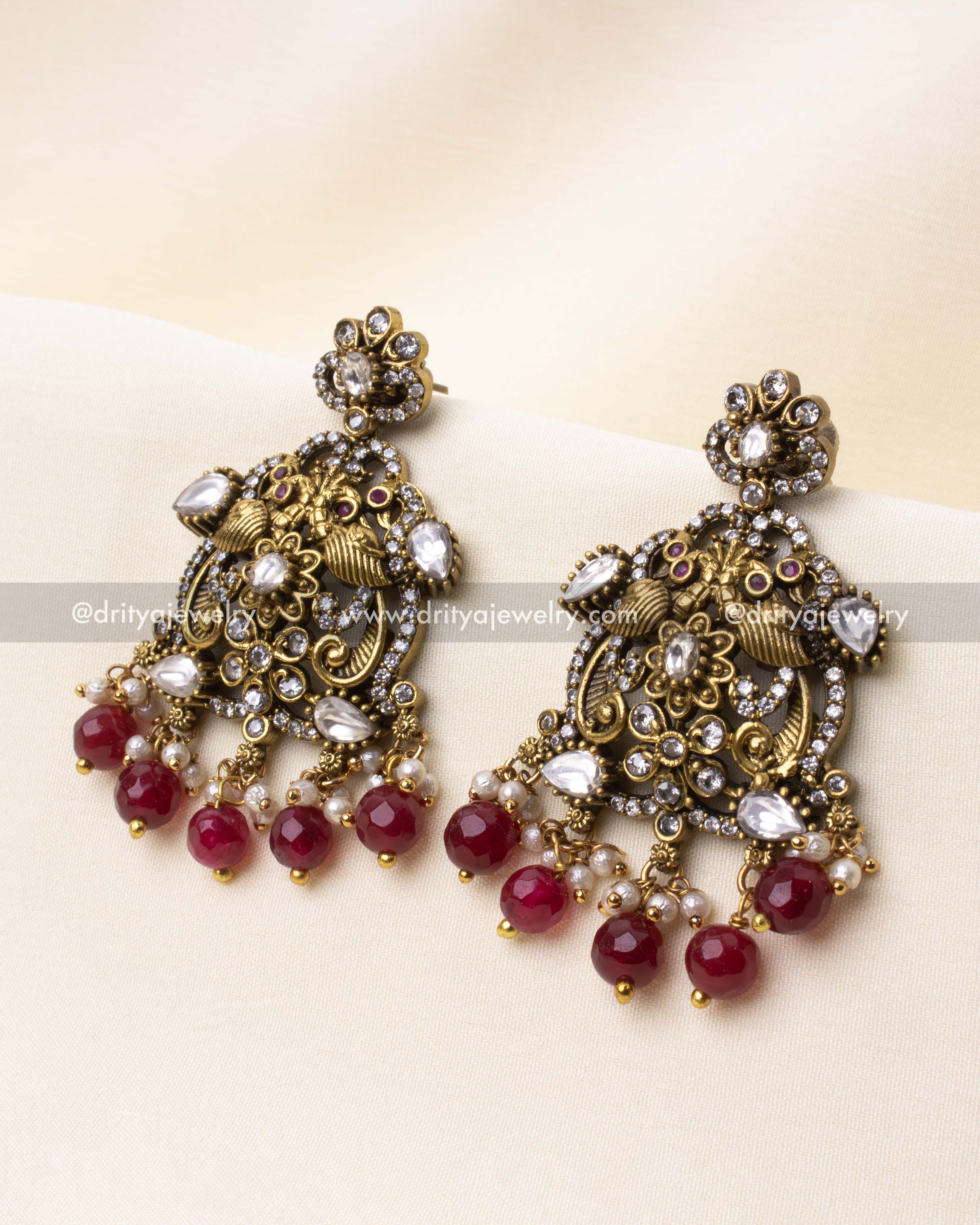 Elegant chandbali-style earrings with polki stones, ruby beads, and pearl drops in antique gold finish.