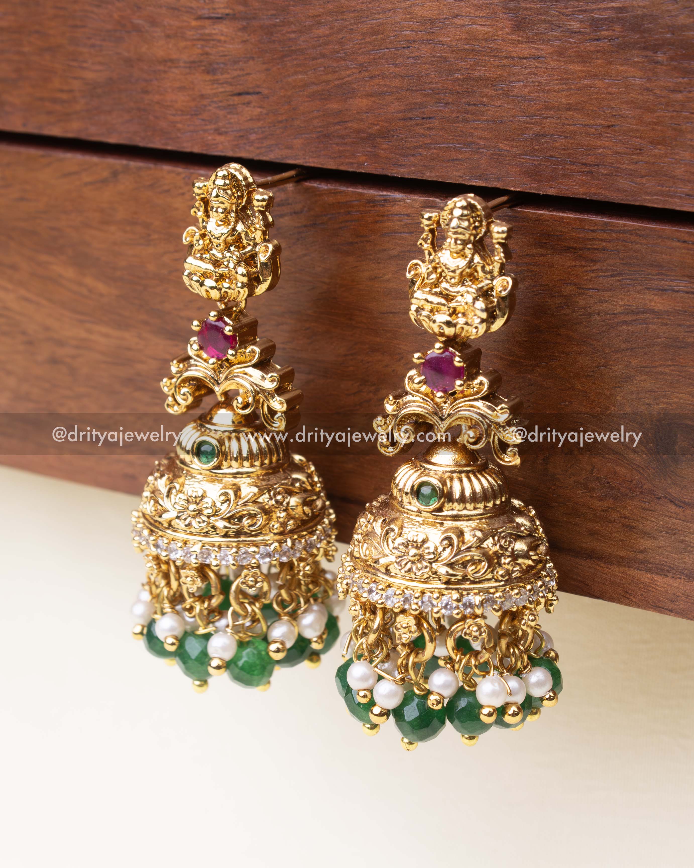 Gold-plated Nakshi jhumka earrings with emerald green beads, pearls, and goddess motif.