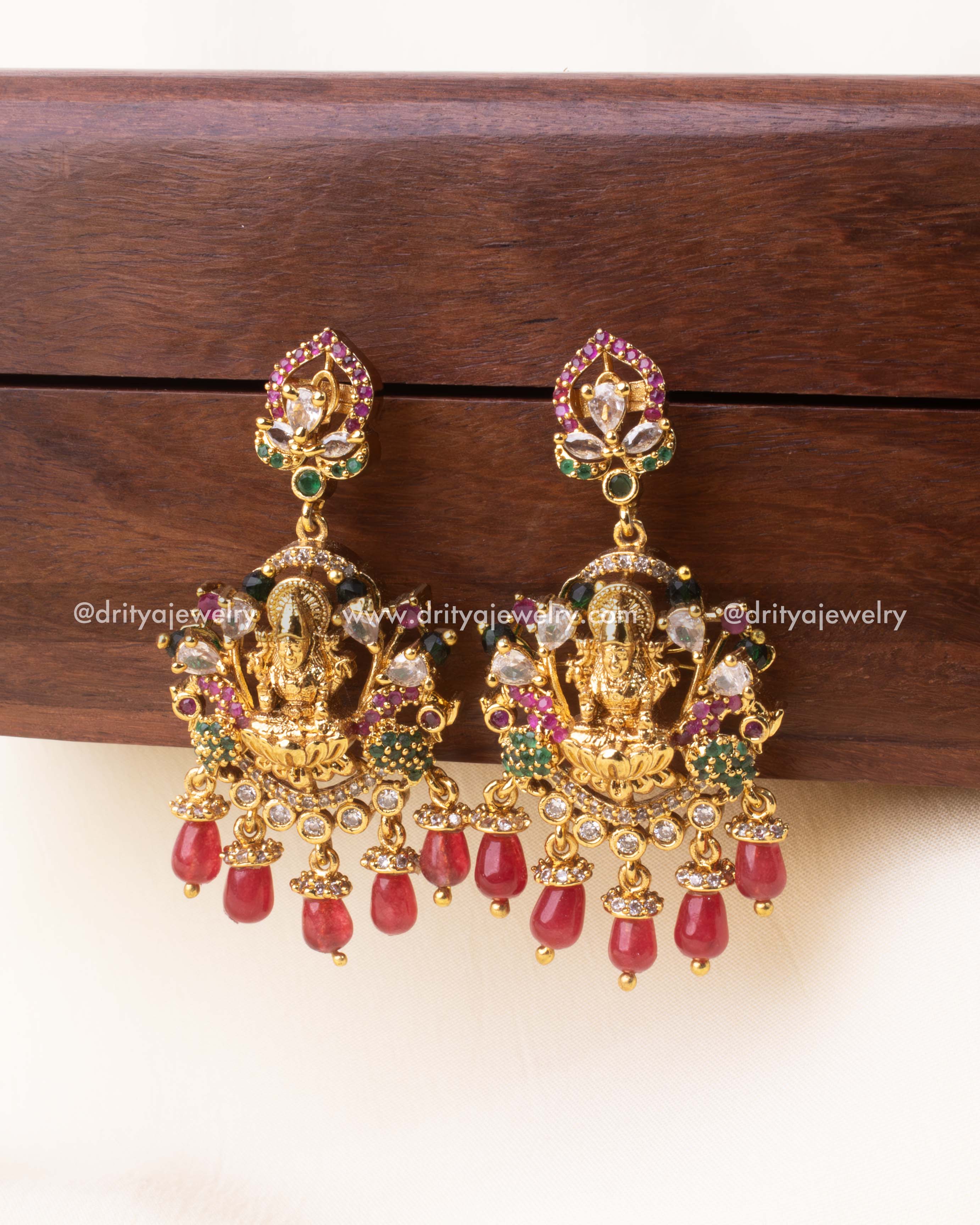 Traditional gold-plated dangler earrings featuring Goddess Lakshmi, red bead hangings, and vibrant stone embellishments.