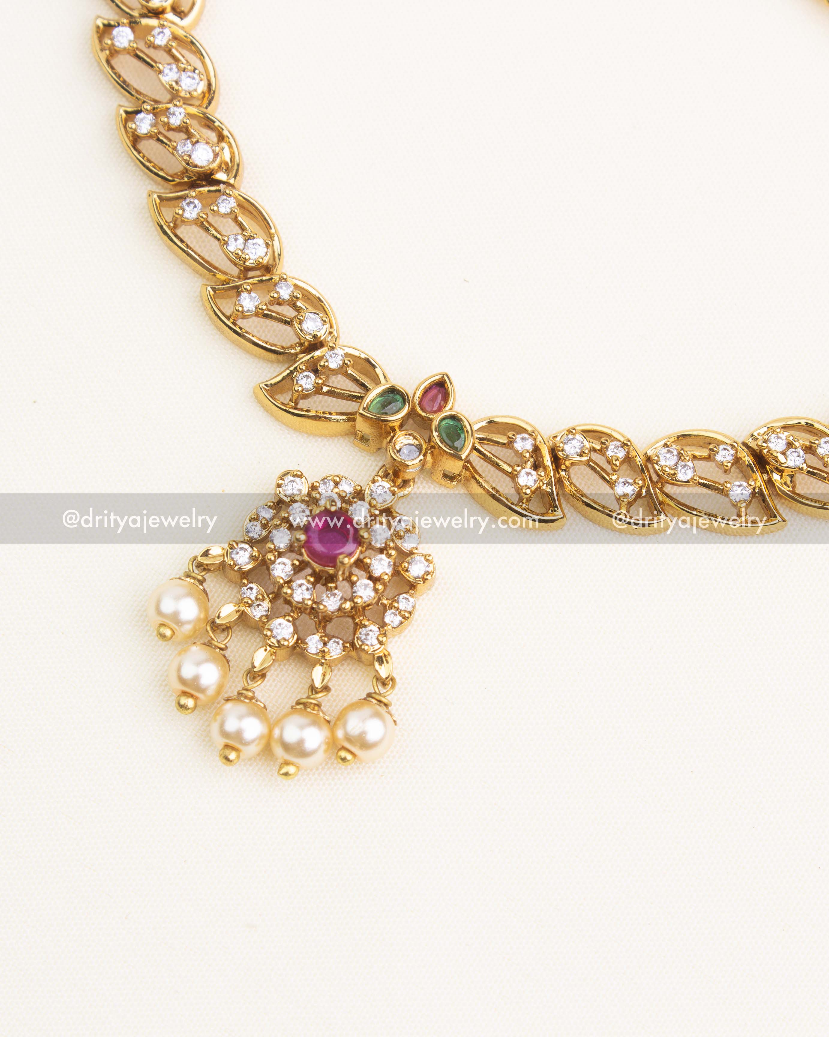Close-up of gold-plated leaf link necklace featuring CZ stones and a ruby-centered floral pendant with pearl drops.