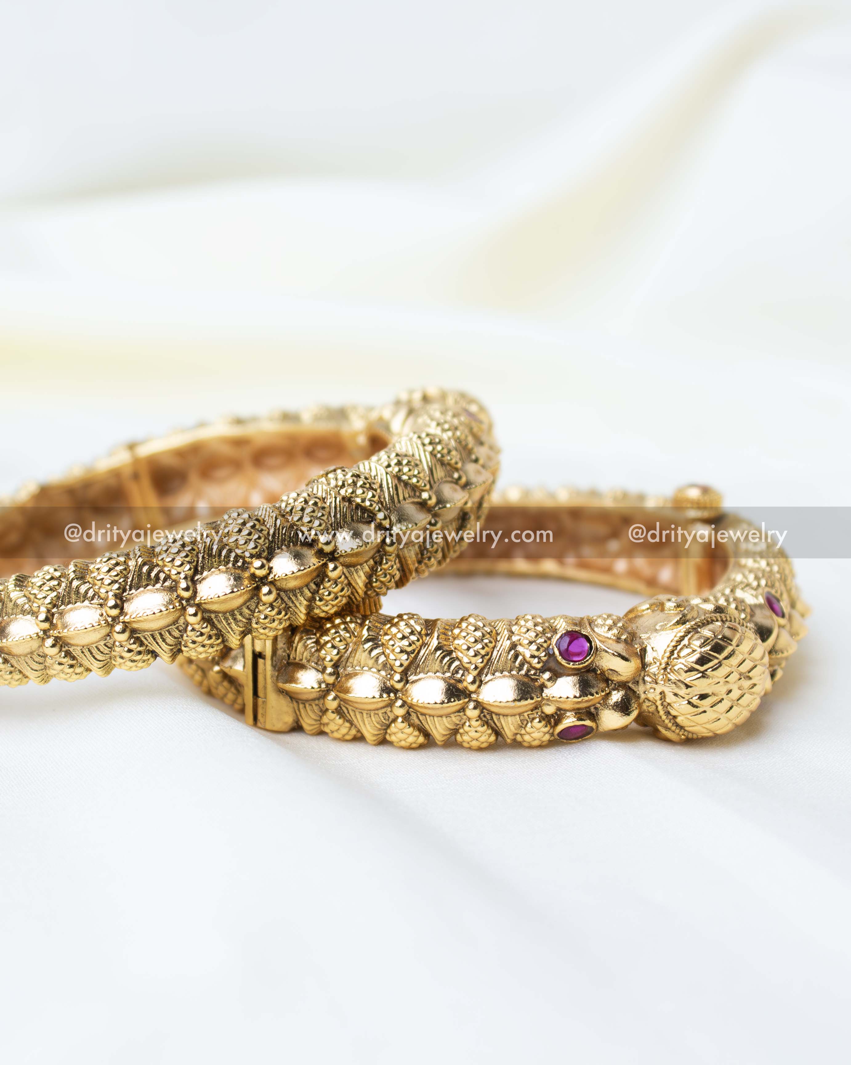 Pair of openable gold-finish kadas with intricate detailing and ruby accents.
