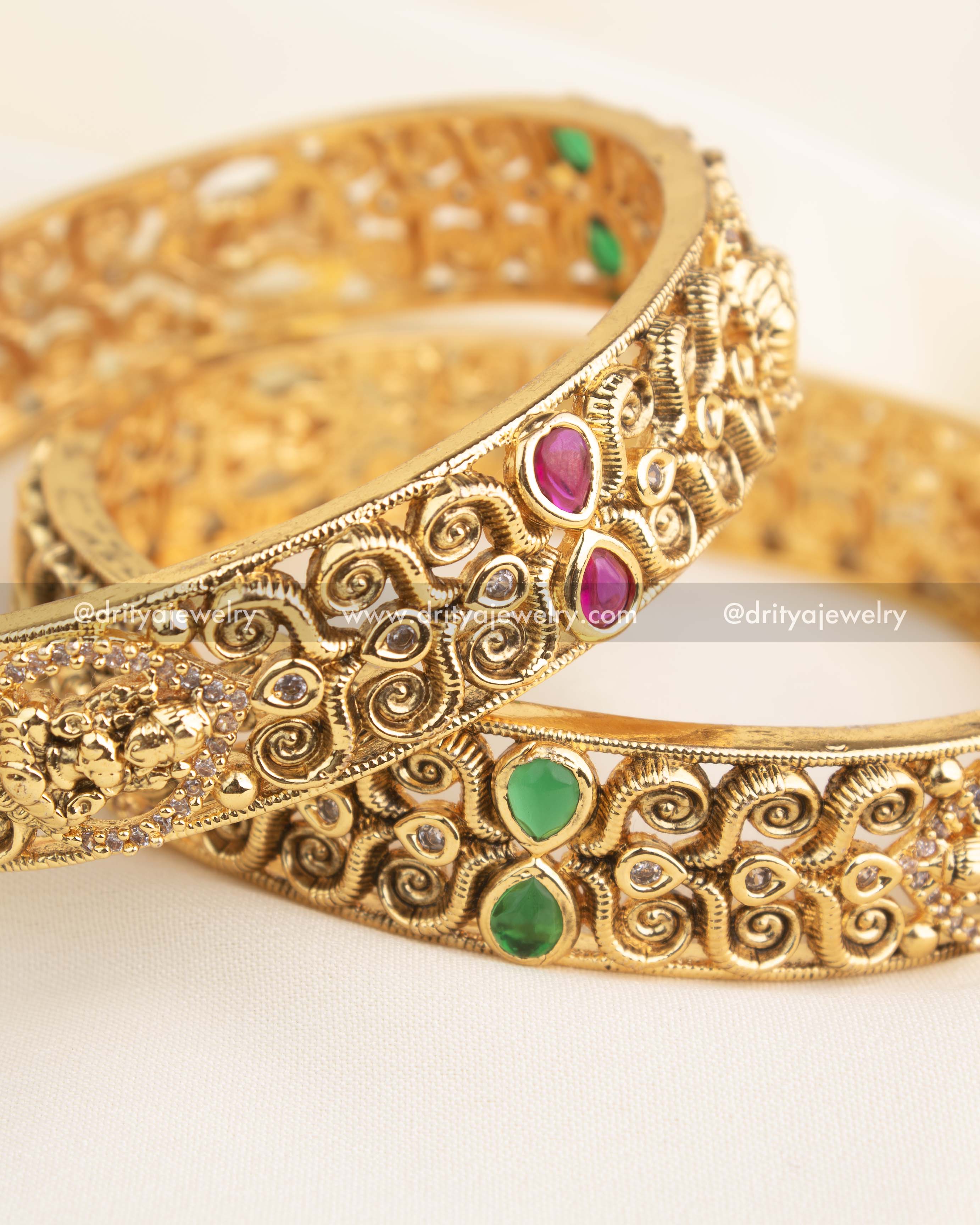 Pair of handcrafted temple bangles with ruby, emerald, and CZ embellishments in antique gold finish.