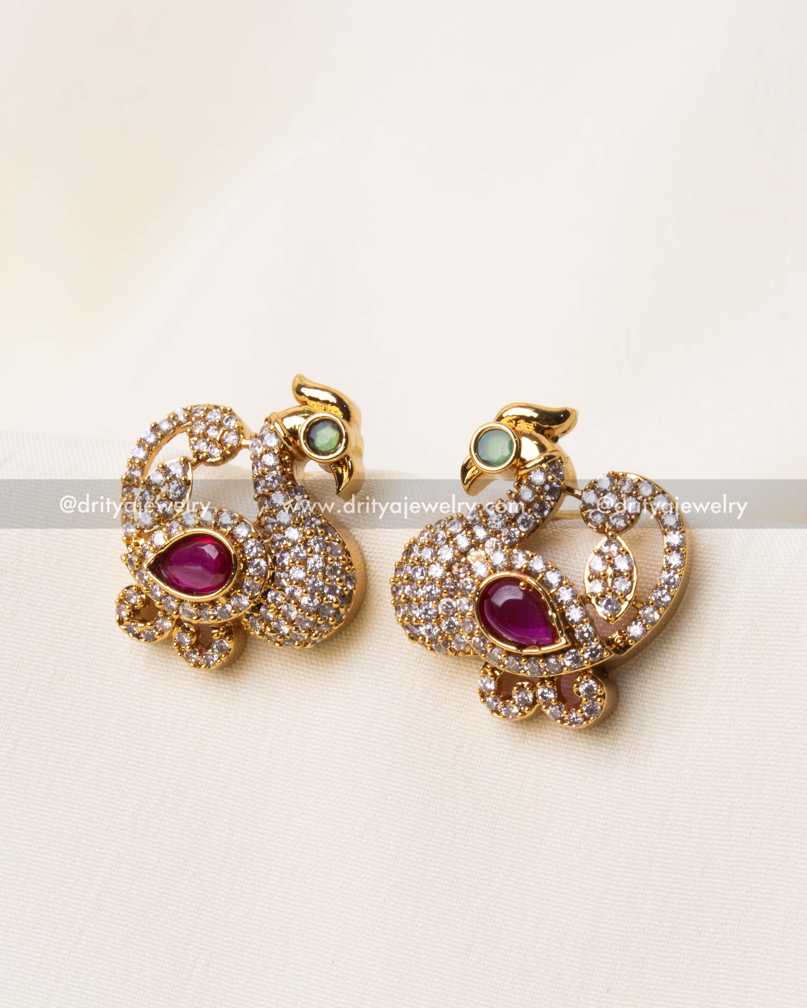 Gold-plated peacock-shaped stud earrings featuring AD stones and a pink gemstone accent.