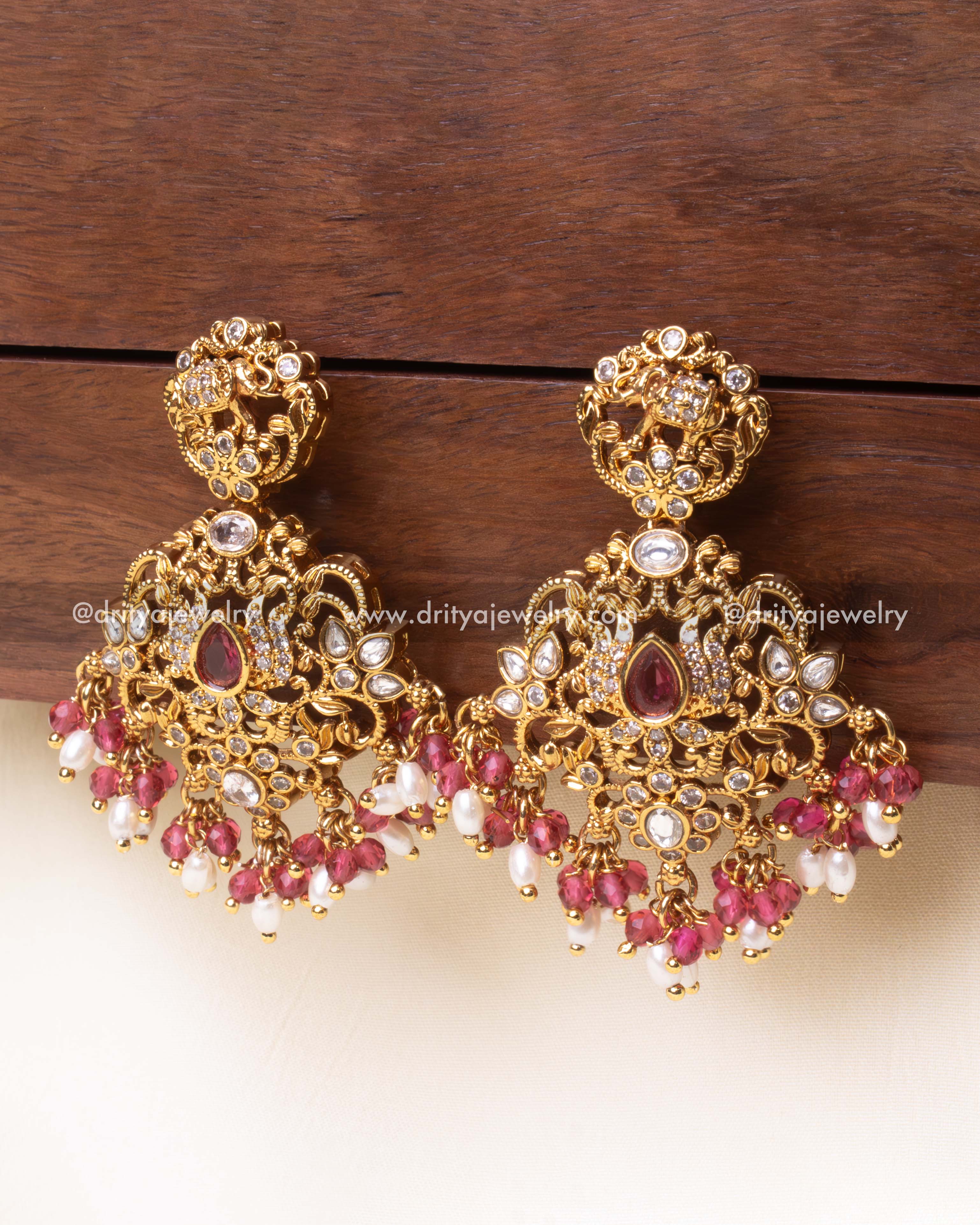 Luxurious gold-plated dangler earrings featuring pink stones, intricate elephant motifs, and pearl bead embellishments.