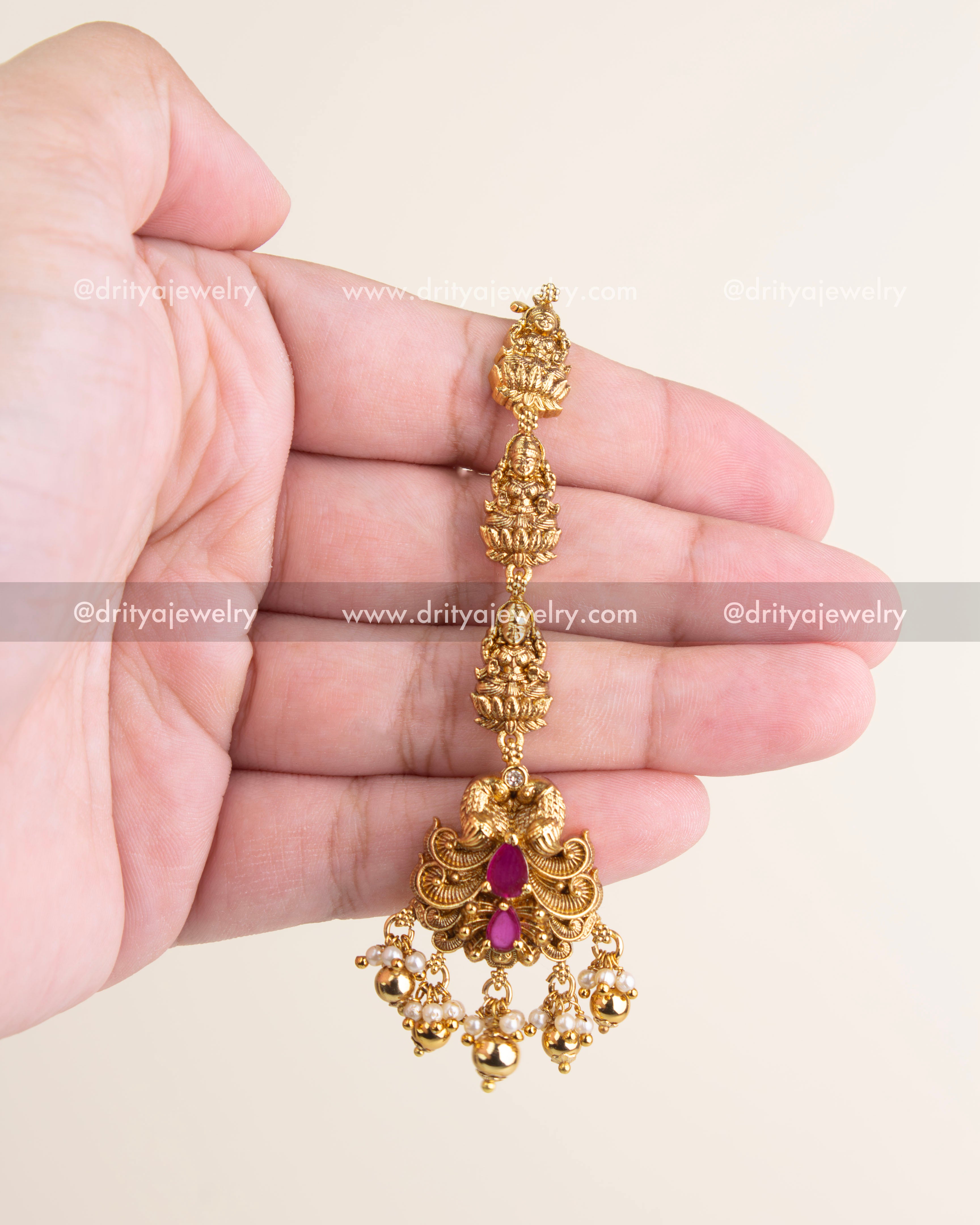 Antique maang tikka with ruby red stones, temple-style nakshi work, and pearl drops, ideal for brides and festive occasions.
