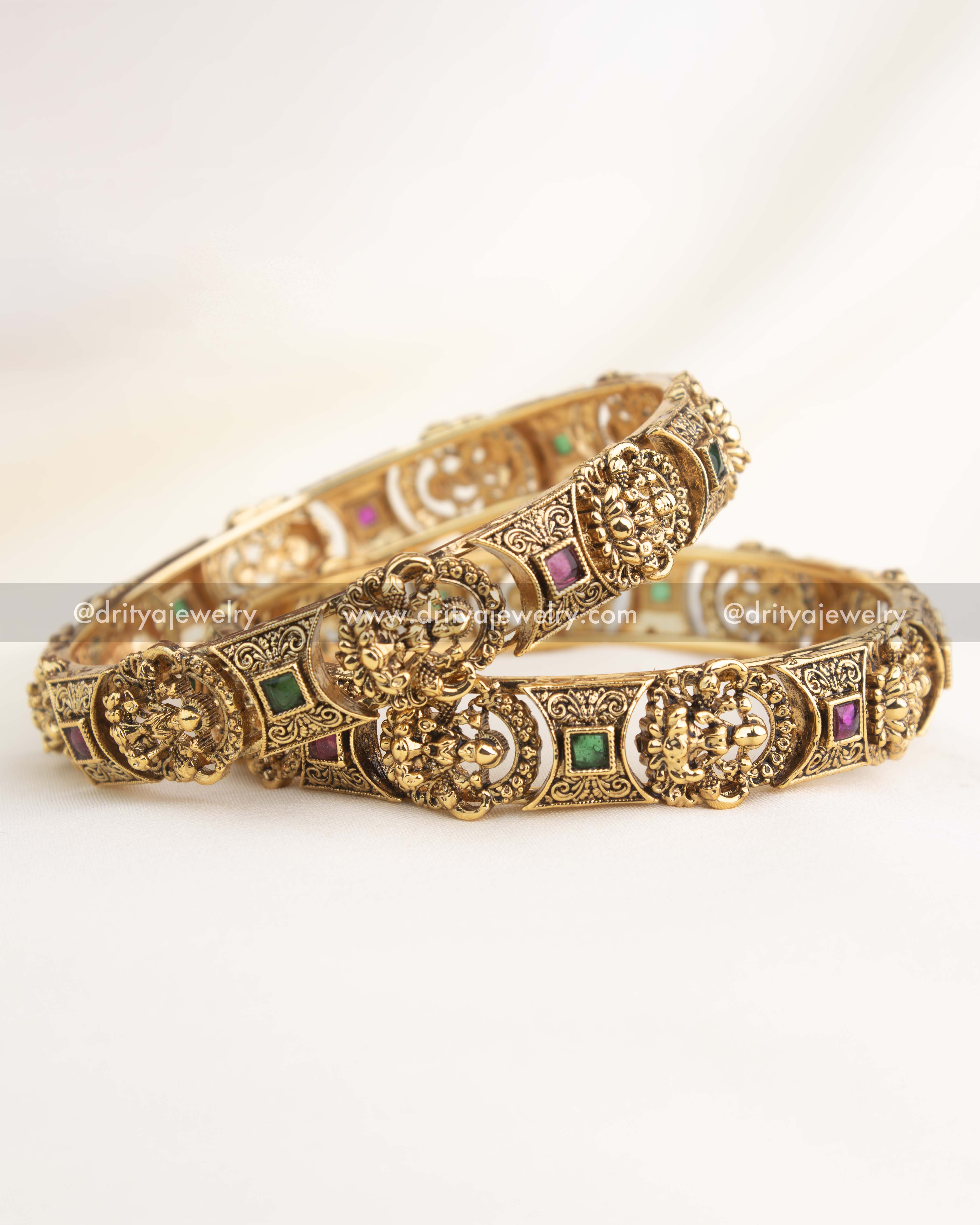 Antique gold temple bangles with intricate goddess engravings and ruby–emerald accents by Dritya Jewelry.