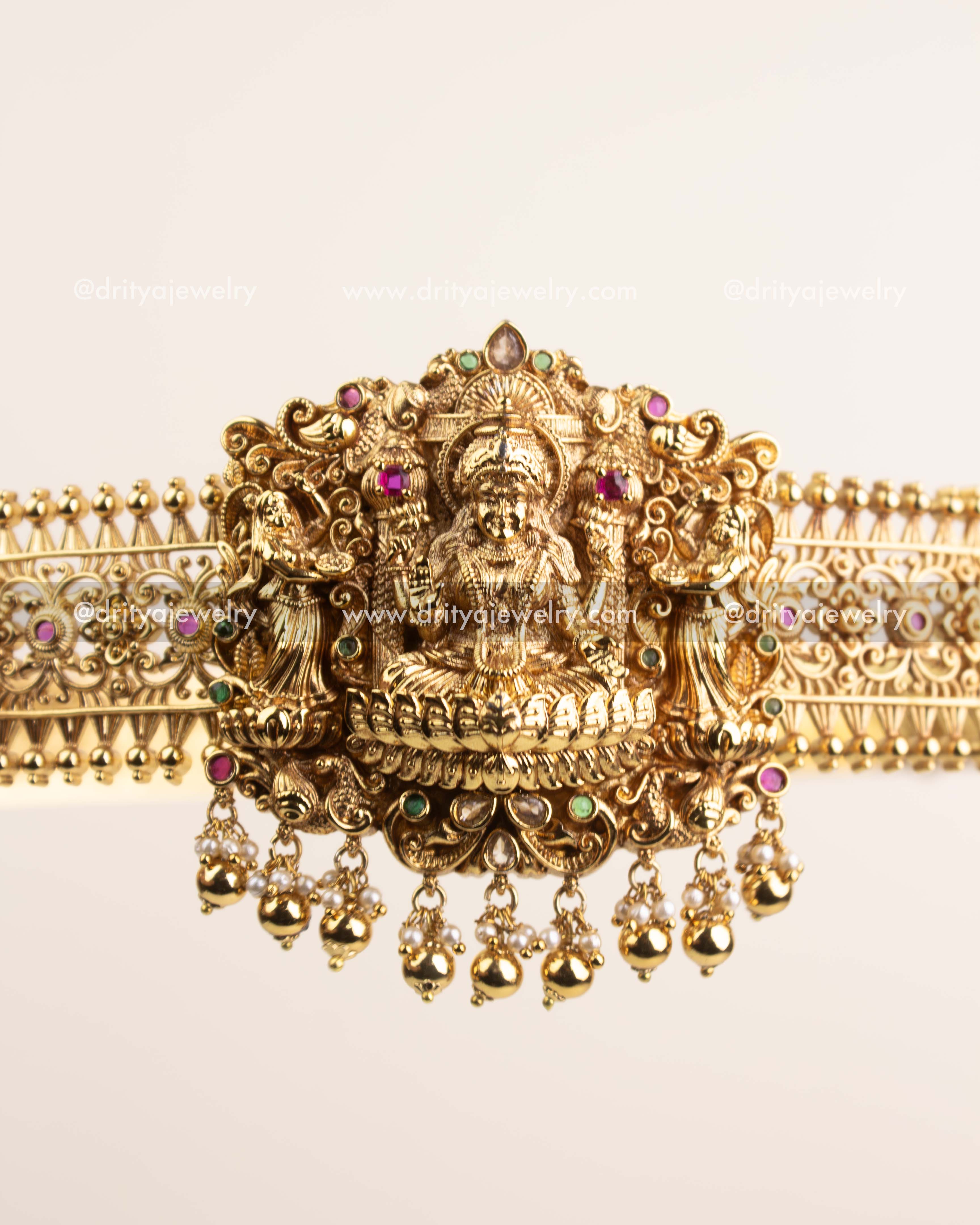 Intricate Nakshi carvings with ruby and emerald accents on antique gold waist belt.