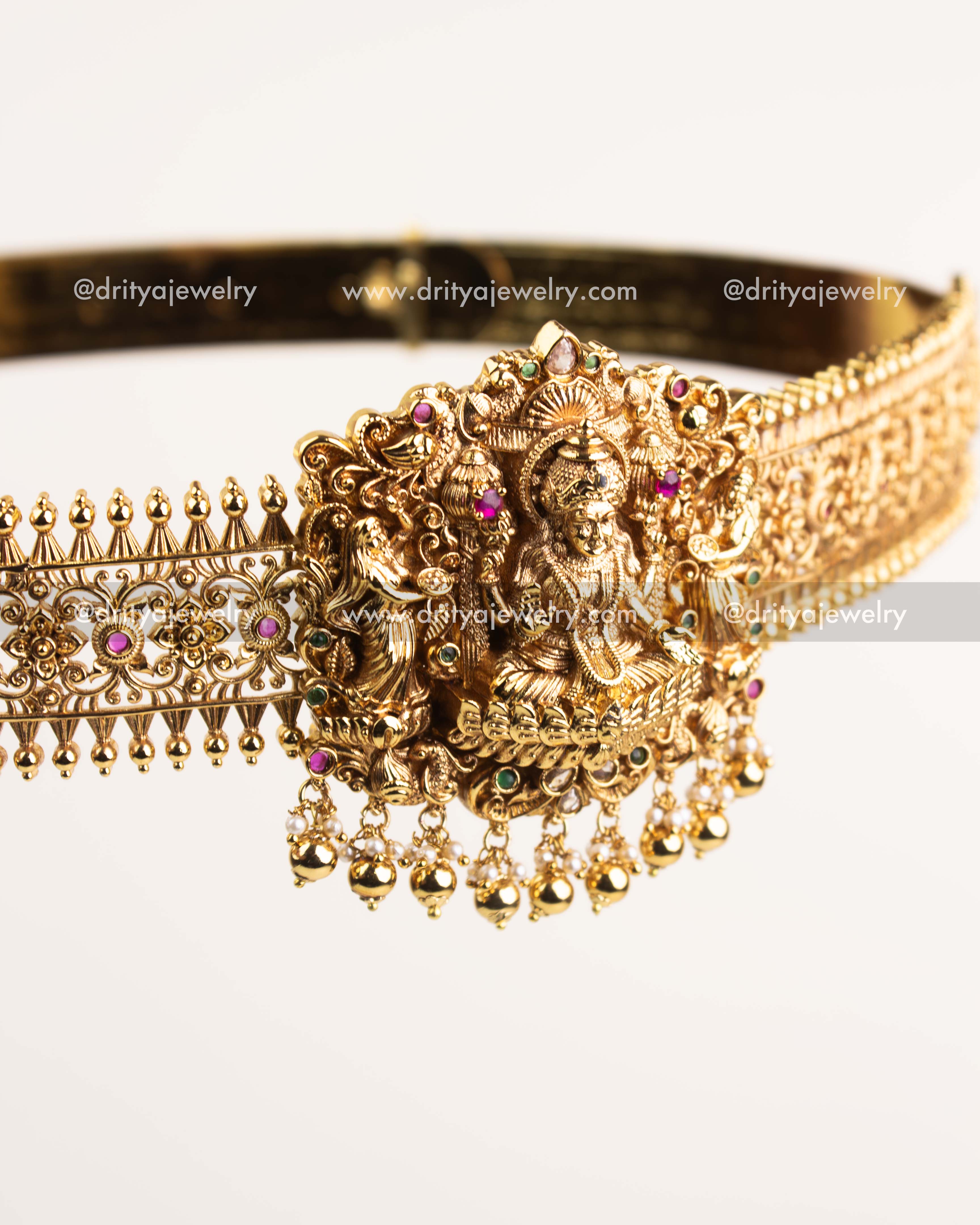 Intricate Nakshi carvings with ruby and emerald accents on antique gold waist belt.