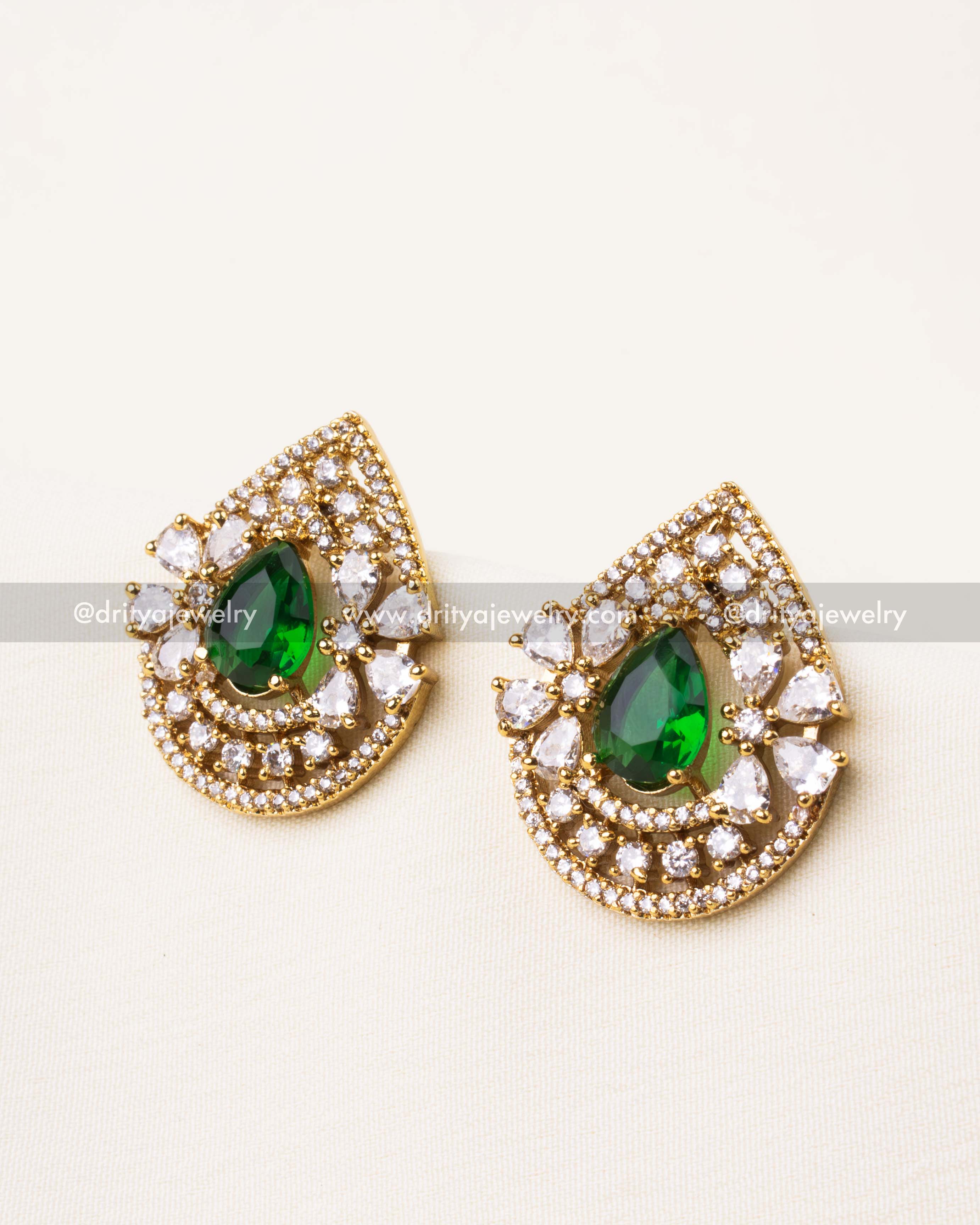 Premium emerald green teardrop CZ stud earrings with halo design and white stones.