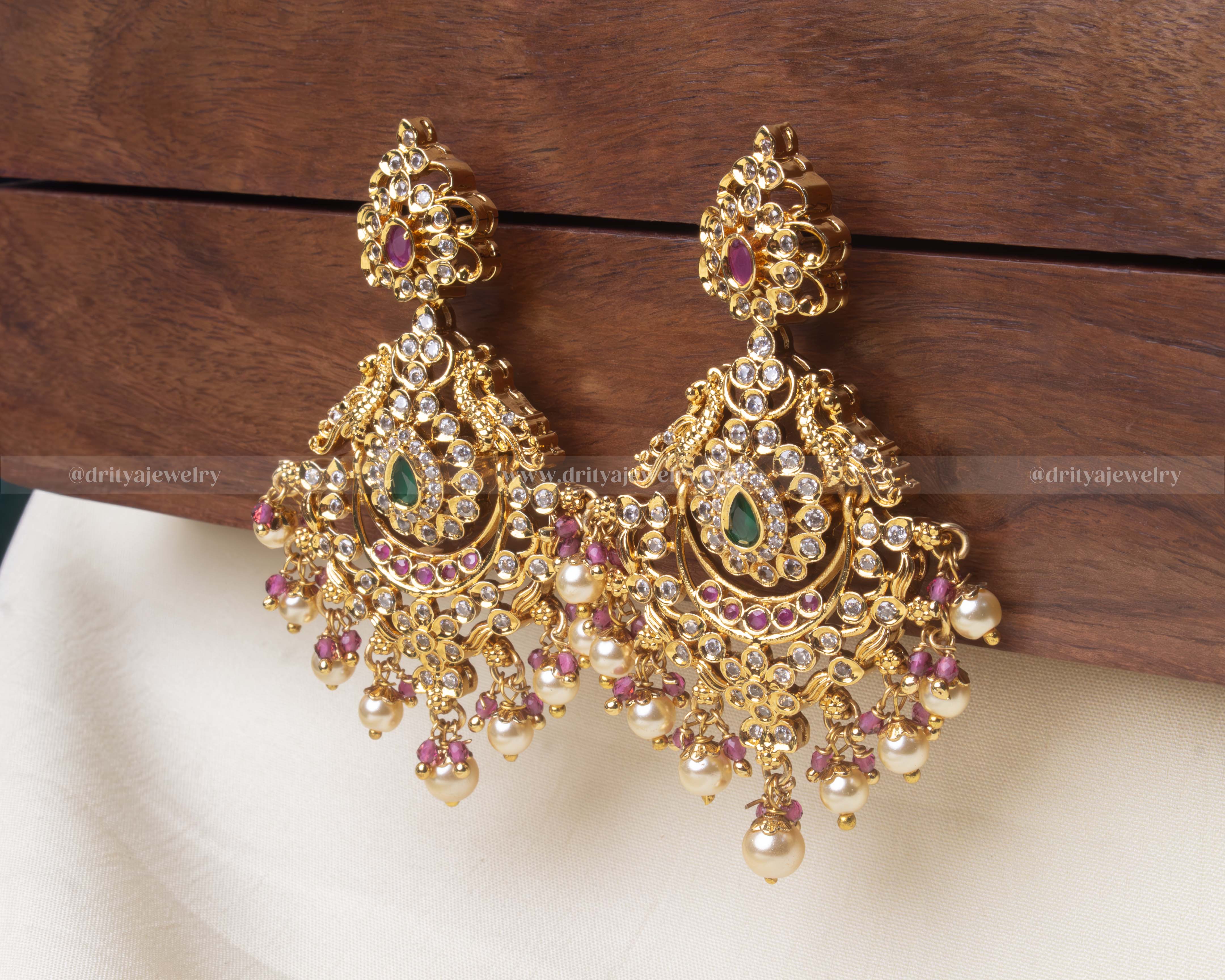 Elegant premium dangler earrings featuring green and ruby accents, cubic zirconia detailing, and hanging pearl embellishments.